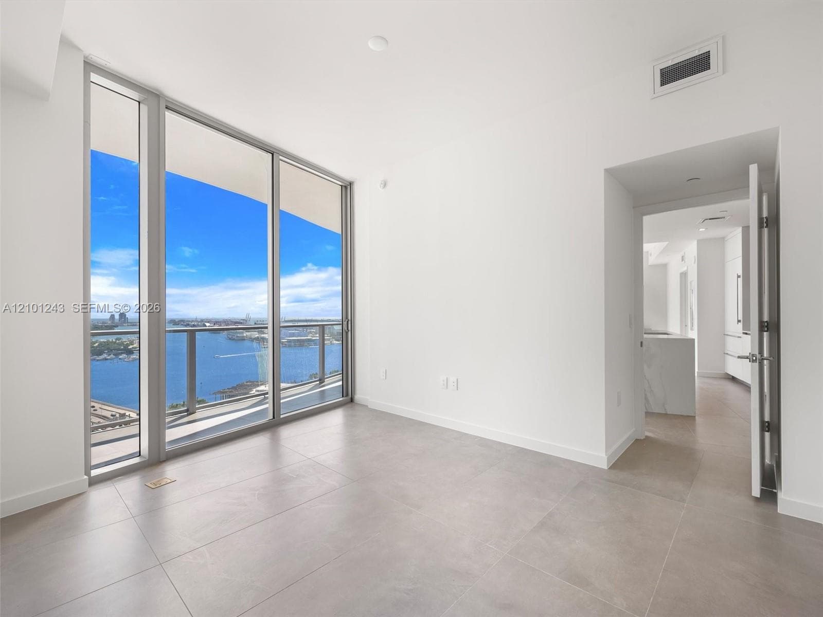 Floor-to-ceiling glass windows, private balcony, neutral tile flooring, and metal-framed sliding glass doors