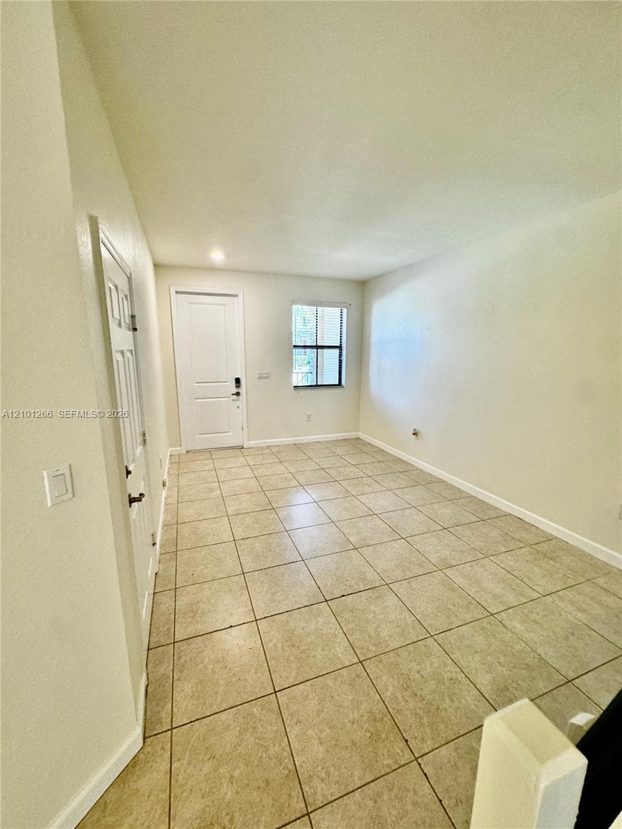 Neutral-toned interior space featuring large-format ceramic tile flooring, a recessed entry door, and a single-pane window with grid detailing