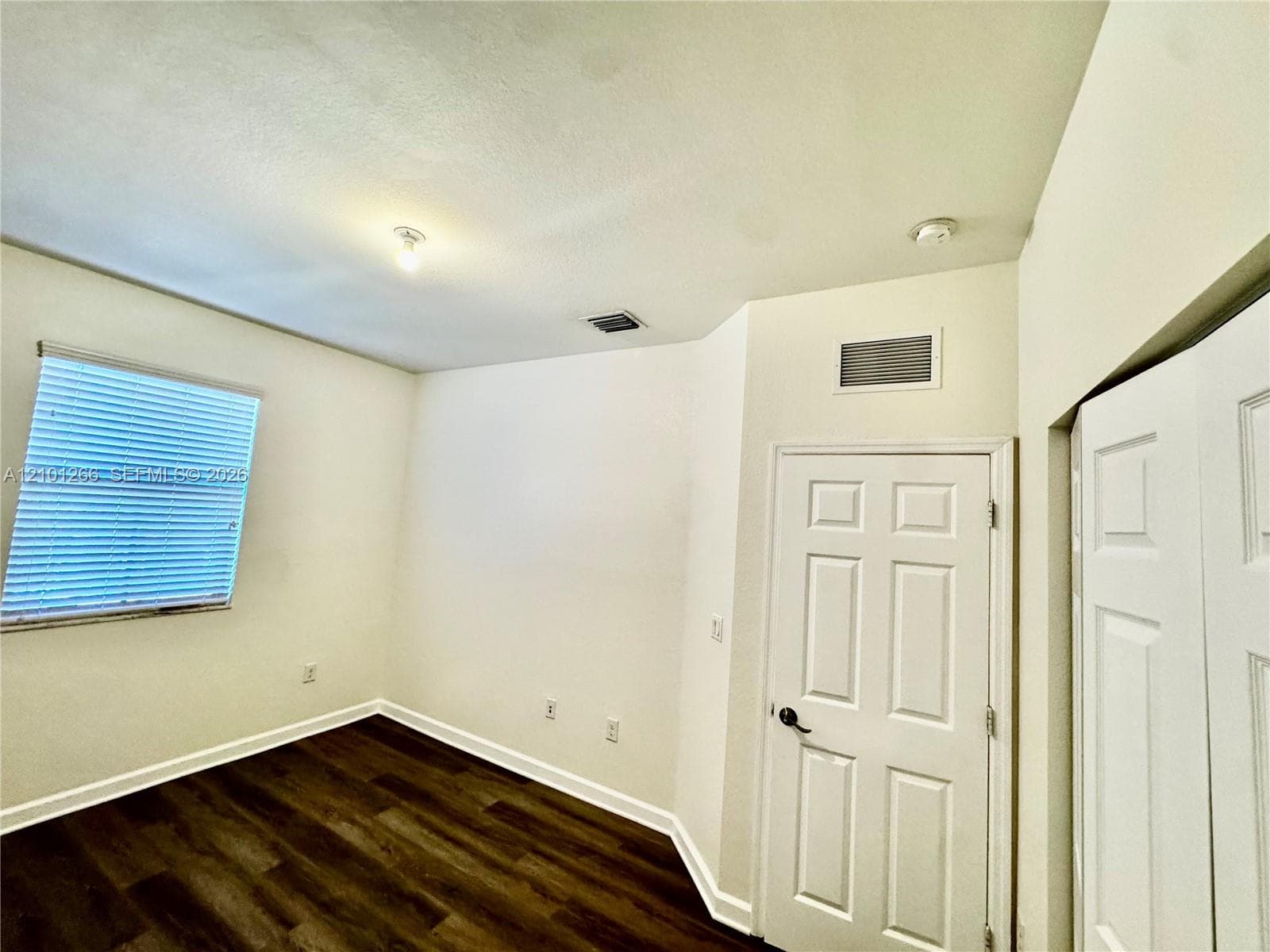 Room featuring wood-finish flooring, a six-panel interior door, and a window with integrated blinds