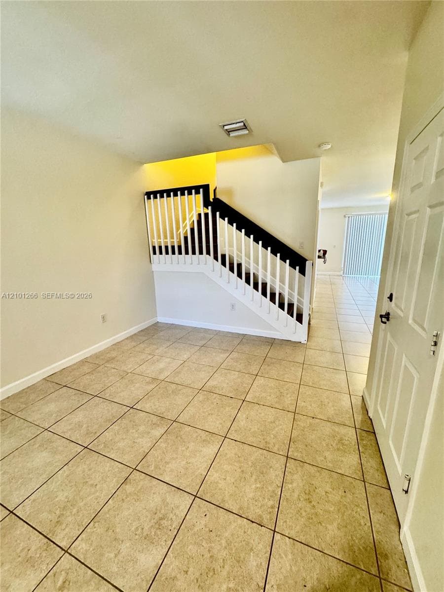 Interior space featuring neutral-toned tile flooring, a staircase with contrasting white spindles and dark handrails, and a multi-panel door