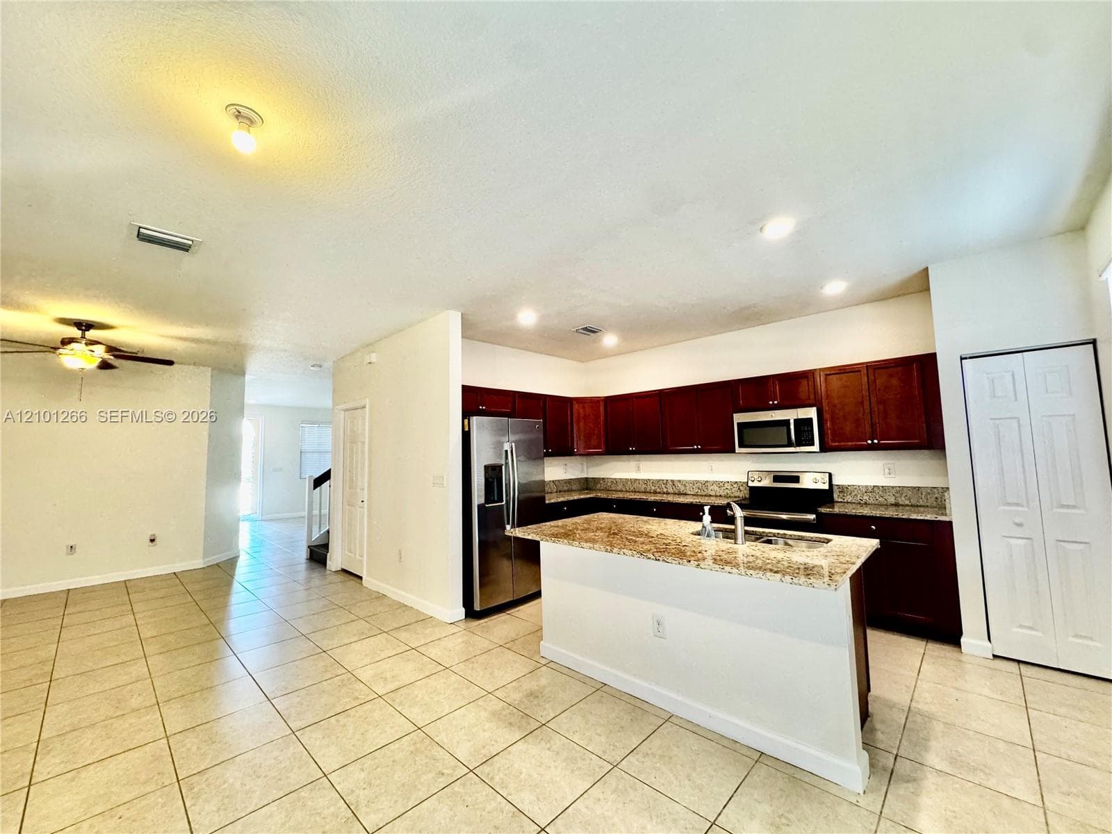 Kitchen featuring dark cabinetry, stone-surface countertops, central island, stainless steel refrigerator, and tiled flooring
