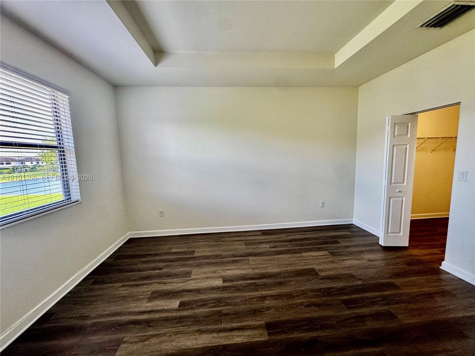 Tray ceiling, wood-finish flooring, and horizontal blind window treatment, with access to a walk-in closet