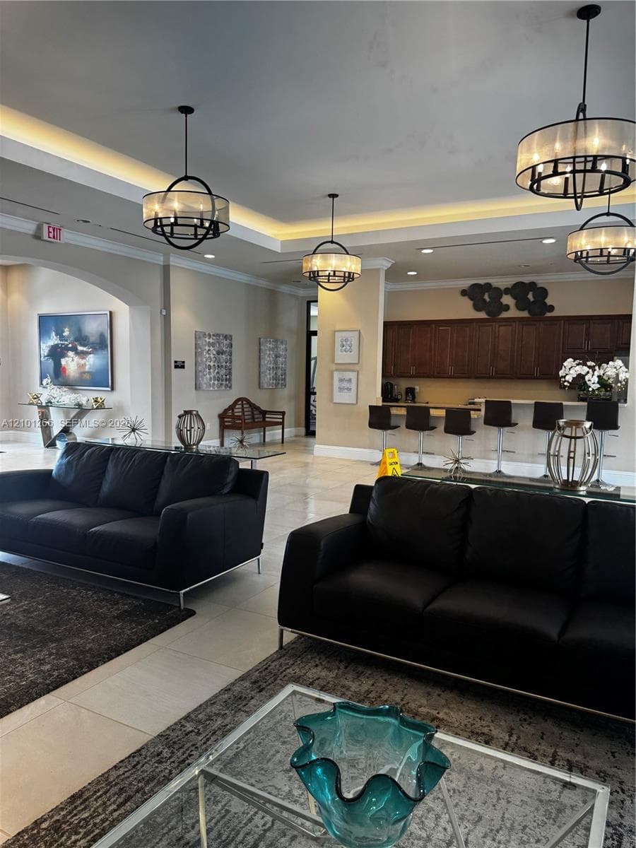 Open concept space featuring recessed tray ceilings with cove lighting, polished tile flooring, dark wood-finish cabinetry, and industrial-style orb chandeliers