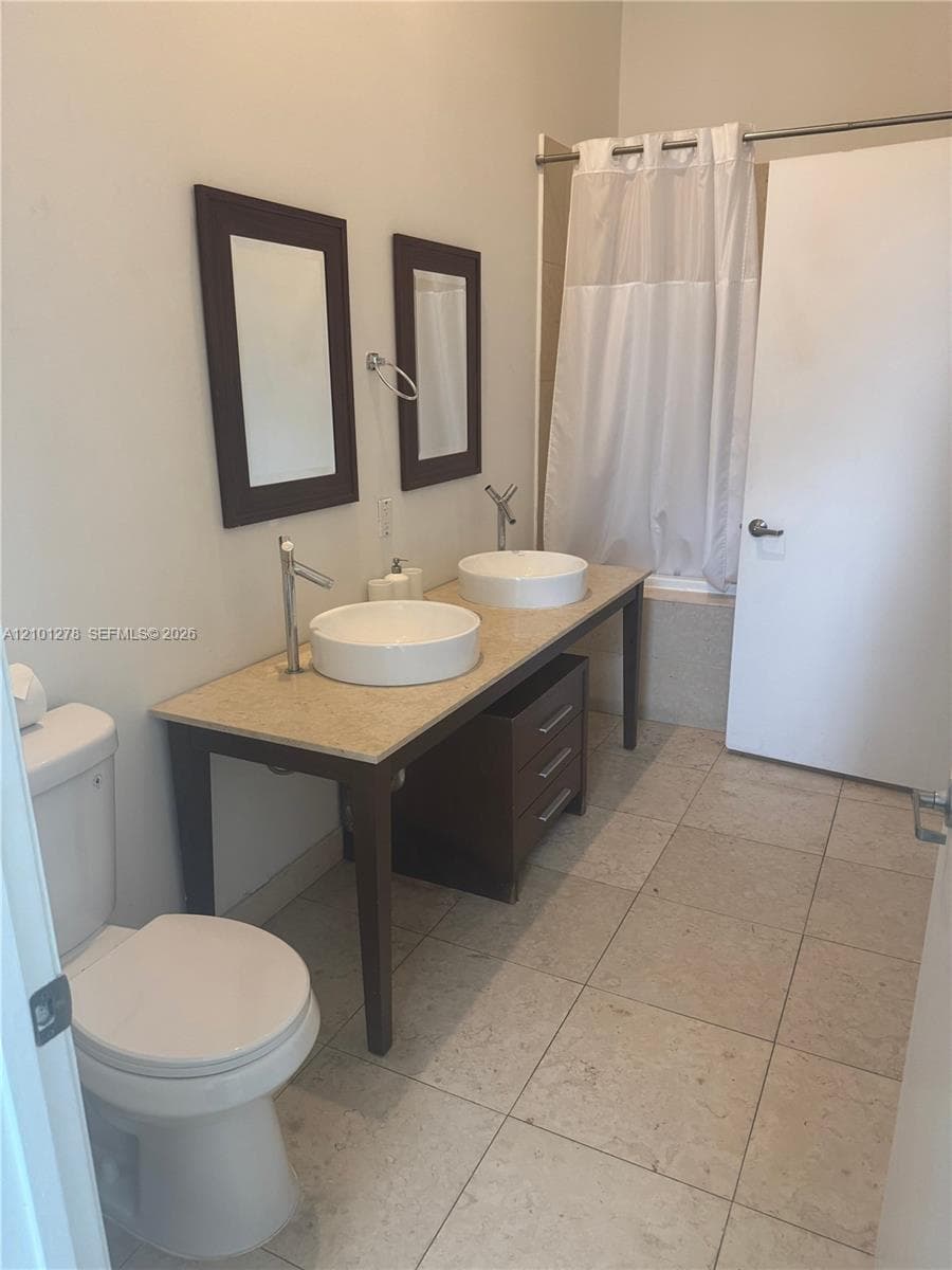 Double vanity featuring vessel sinks, stone-finish countertop, dark wood-tone cabinetry, and large-format tile flooring