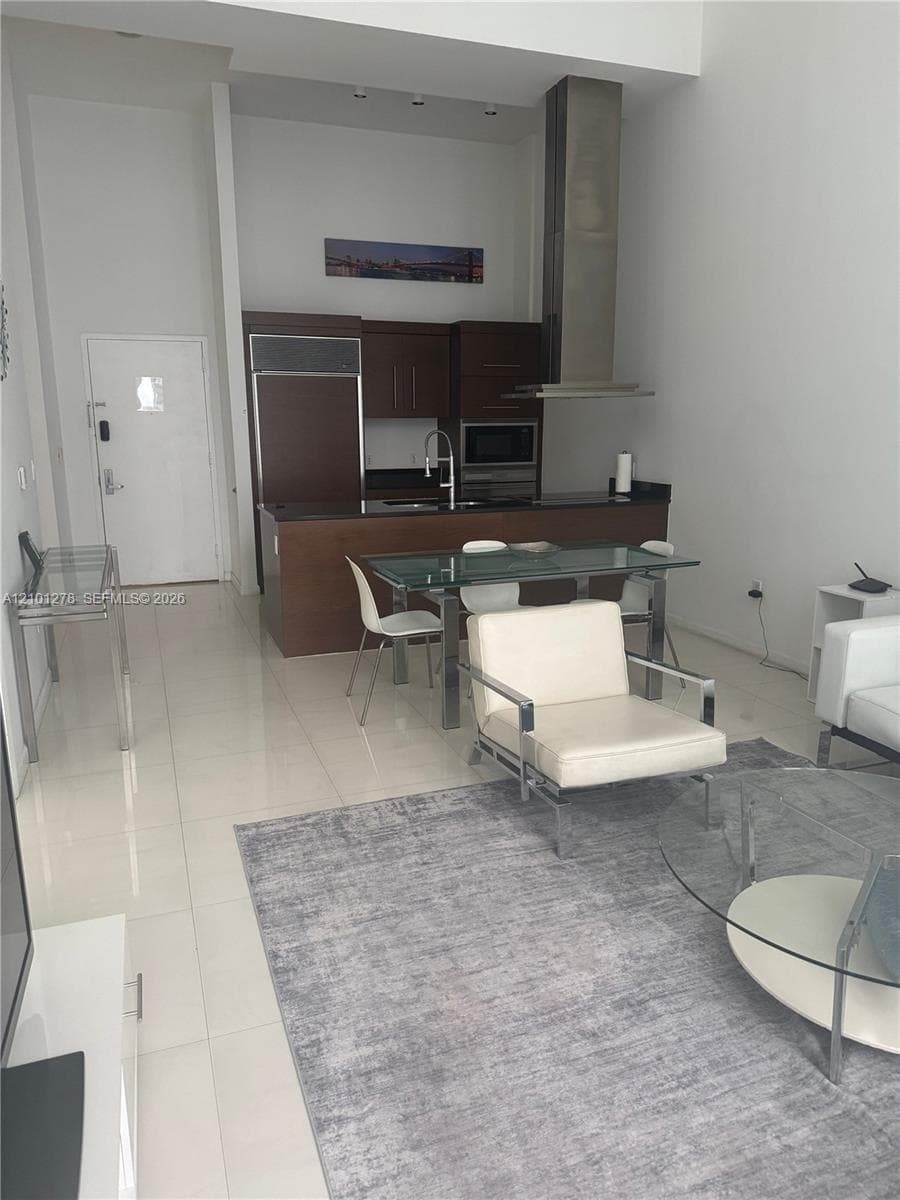 High-ceiling interior featuring flat-panel dark wood cabinetry, stainless steel range hood, stone countertops, and polished tile flooring