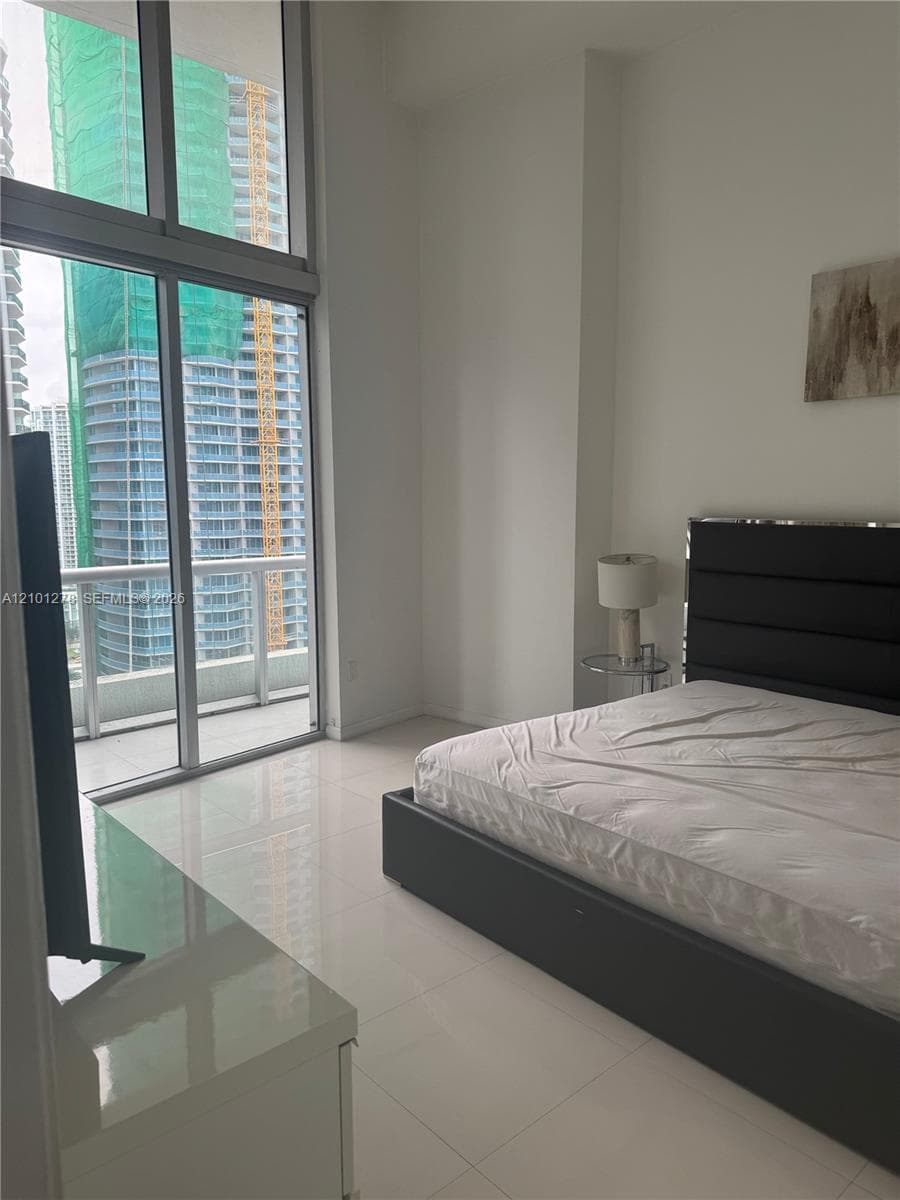 Floor-to-ceiling windows, high ceilings, glass-paneled balcony access, and polished tile flooring