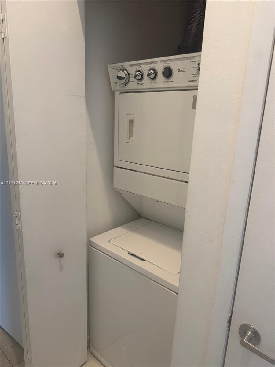 Stacked laundry unit featuring a white top-loading washer and front-loading dryer enclosed within a closet