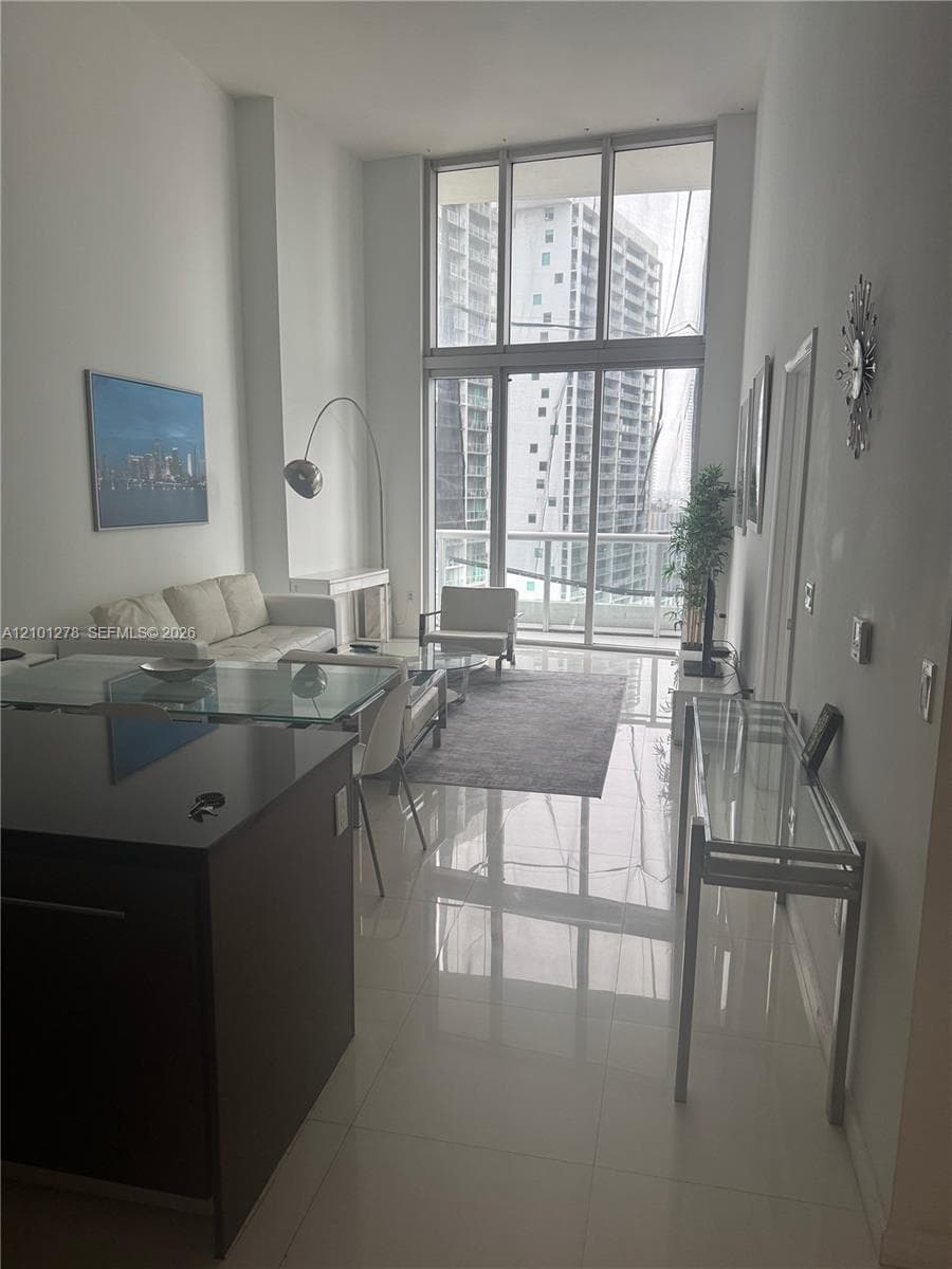 Double-height floor-to-ceiling windows, polished tile flooring, glass-railed balcony, and dark-toned kitchen cabinetry