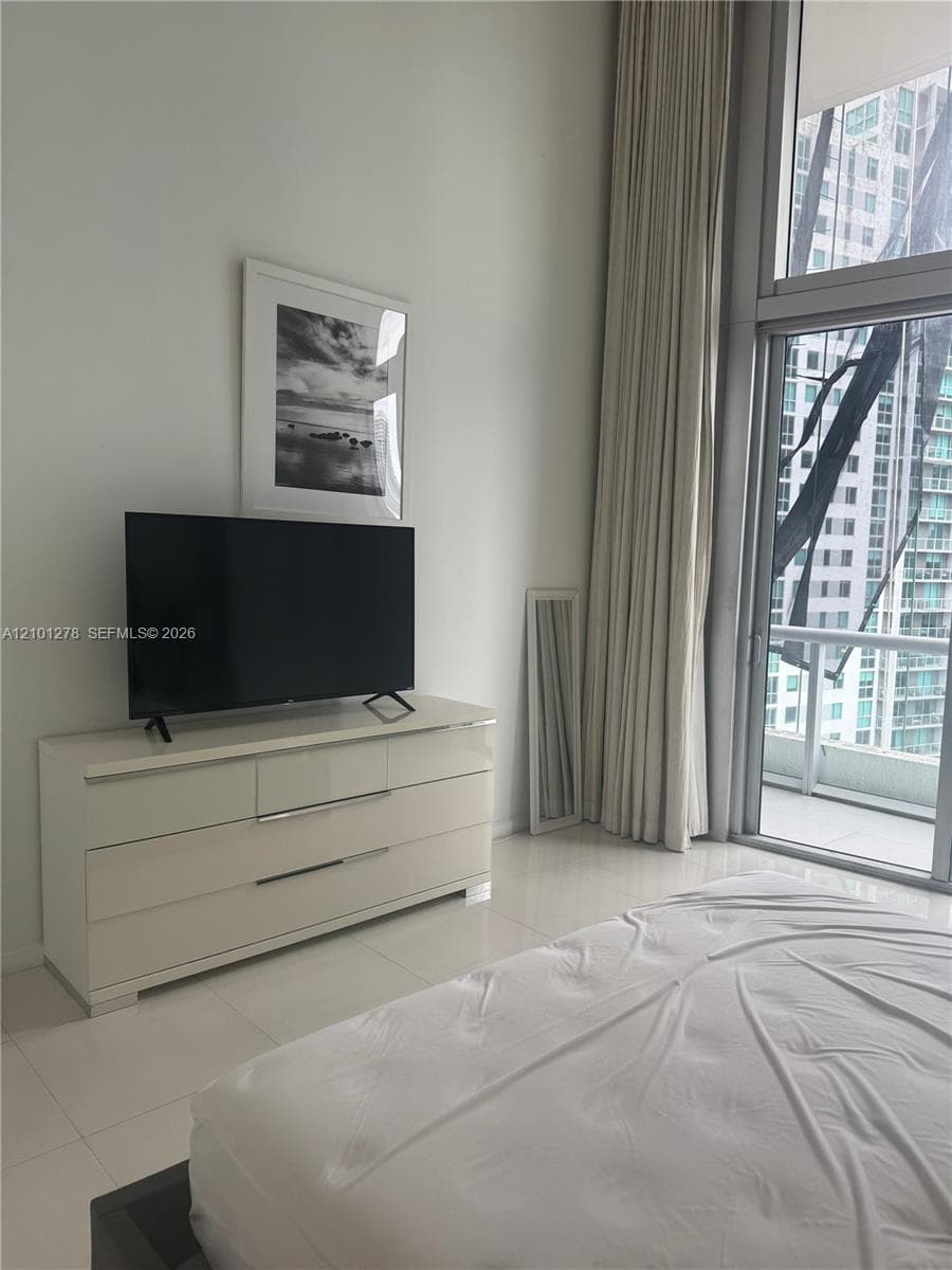 Floor-to-ceiling windows, white tile flooring, and a private balcony access point