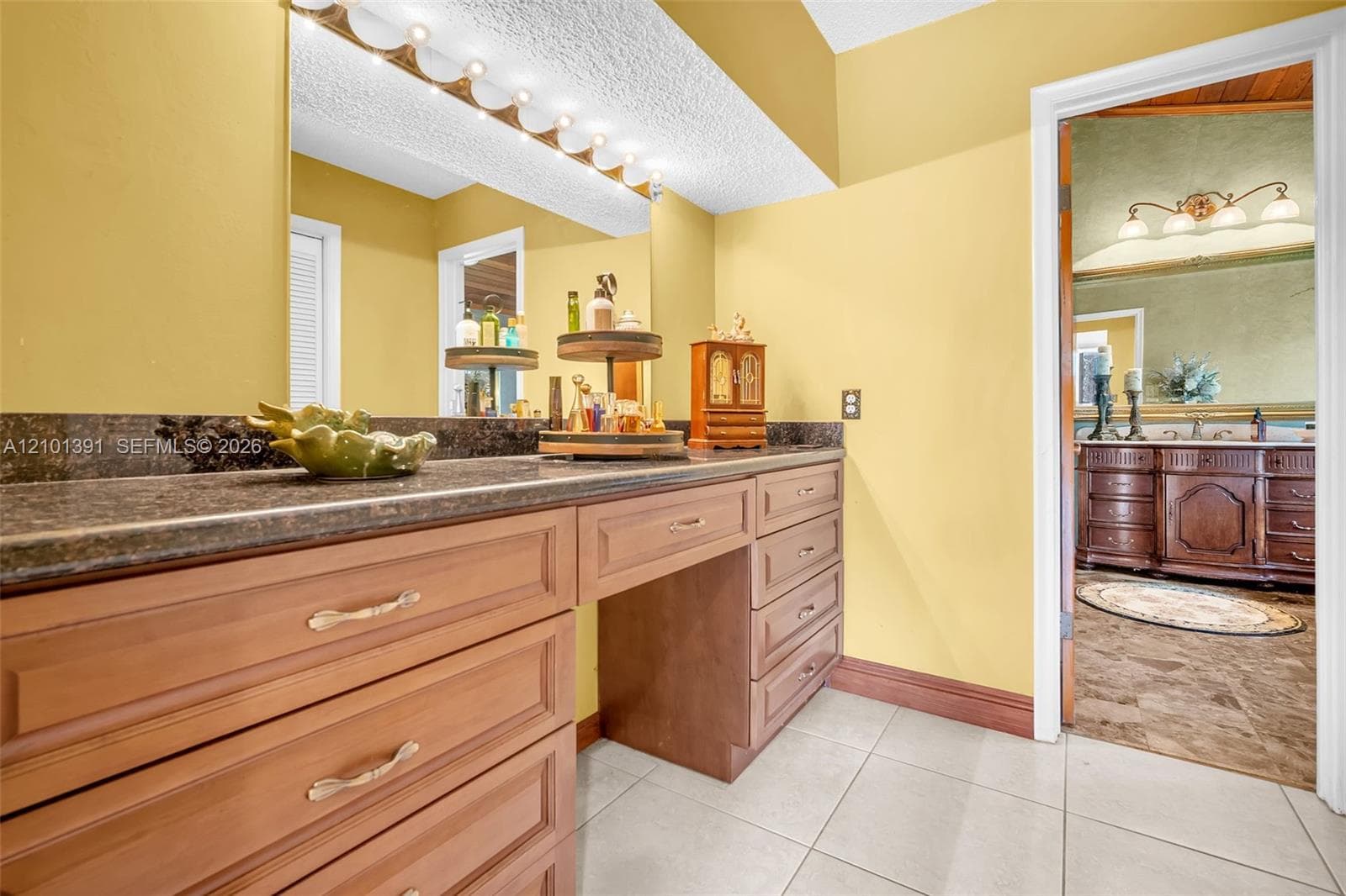 Extended vanity with integrated makeup area, dark stone countertop, and ample storage cabinetry with gold-tone hardware