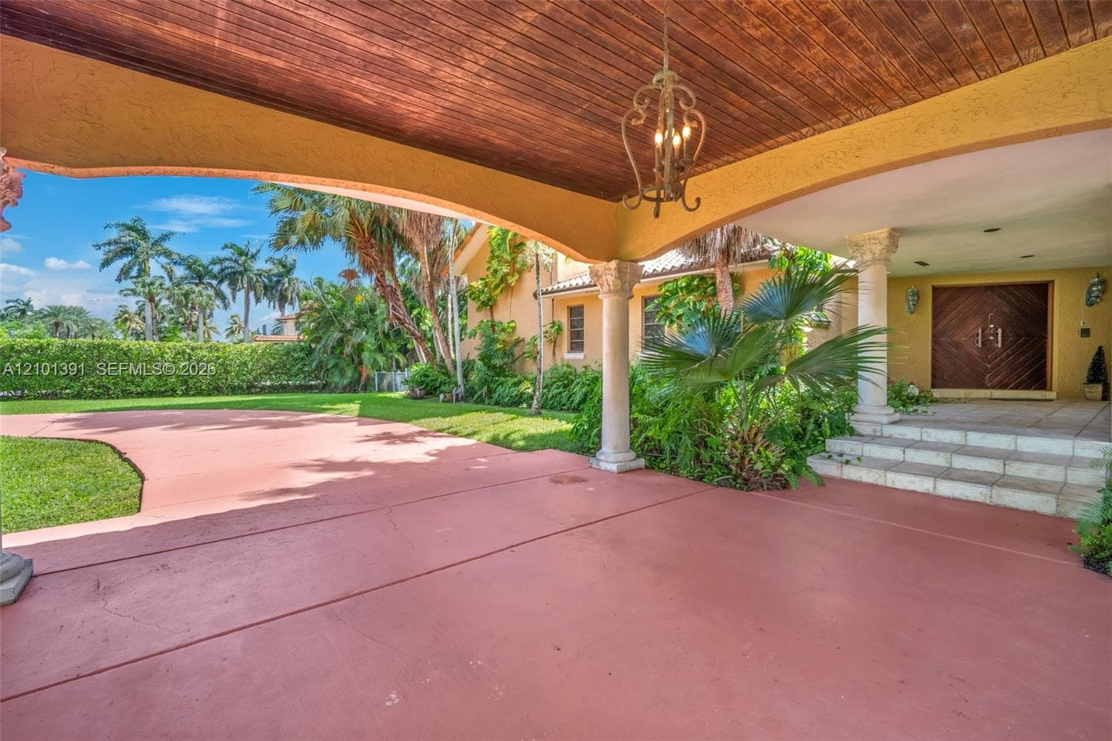 Covered entry with wood-paneled ceiling, decorative chandelier, and stone columns