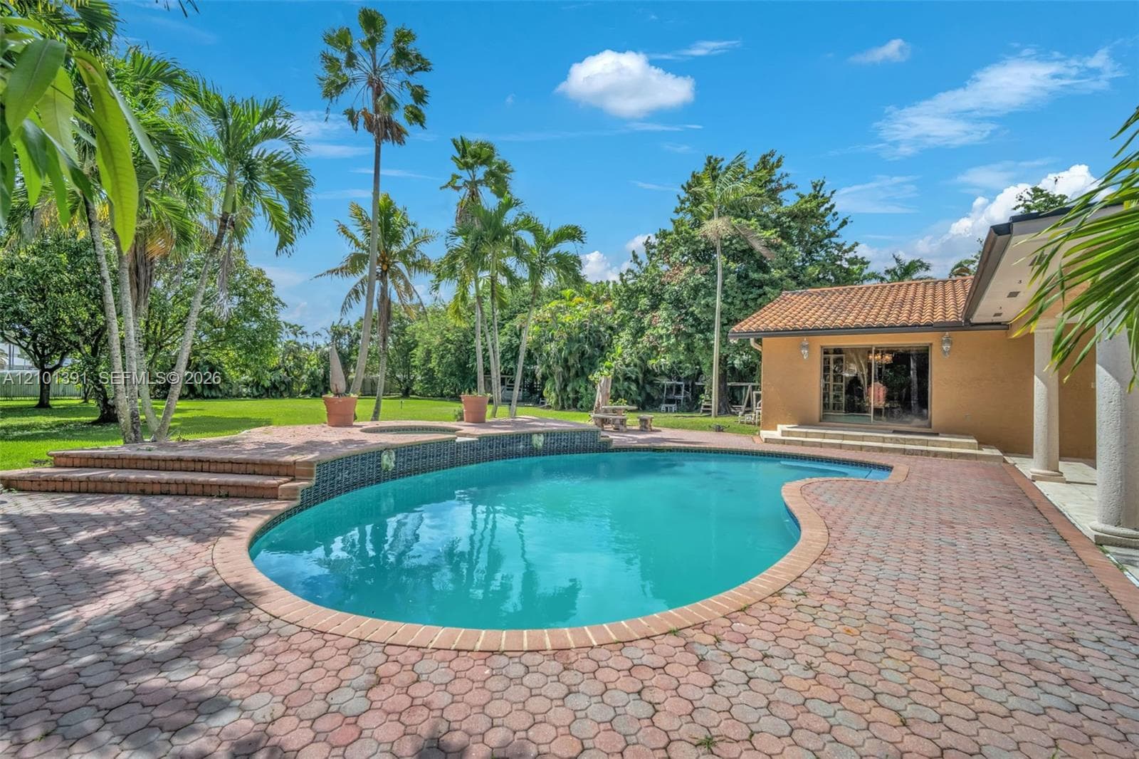 Freeform swimming pool with a textured tile border, surrounded by brick paver decking