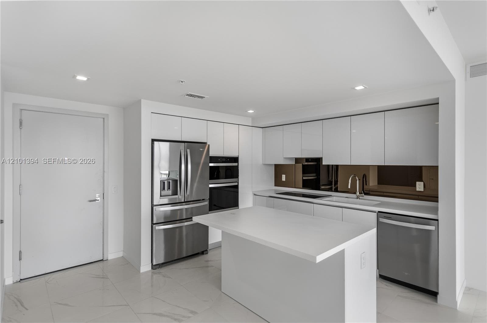 Kitchen featuring white flat-panel cabinetry, a central island with a solid-surface countertop, stainless steel appliances including a built-in wall oven, and a reflective backsplash