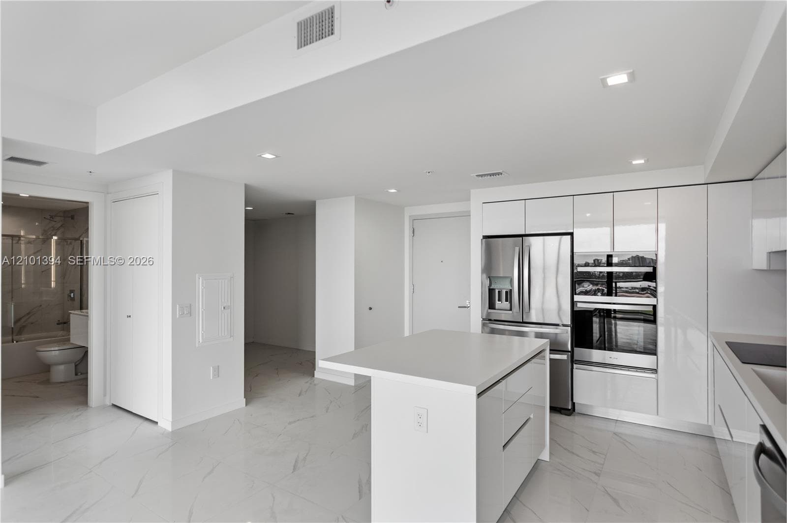 Modern kitchen featuring high-gloss cabinetry, a central island with a solid-surface countertop, stainless steel appliances, integrated double wall ovens, and stone-finish flooring