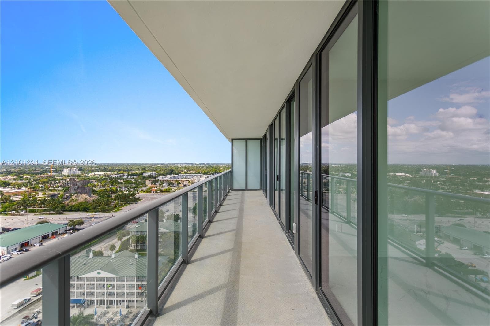 Covered balcony featuring expansive glass railing, floor-to-ceiling sliding glass doors, and concrete flooring