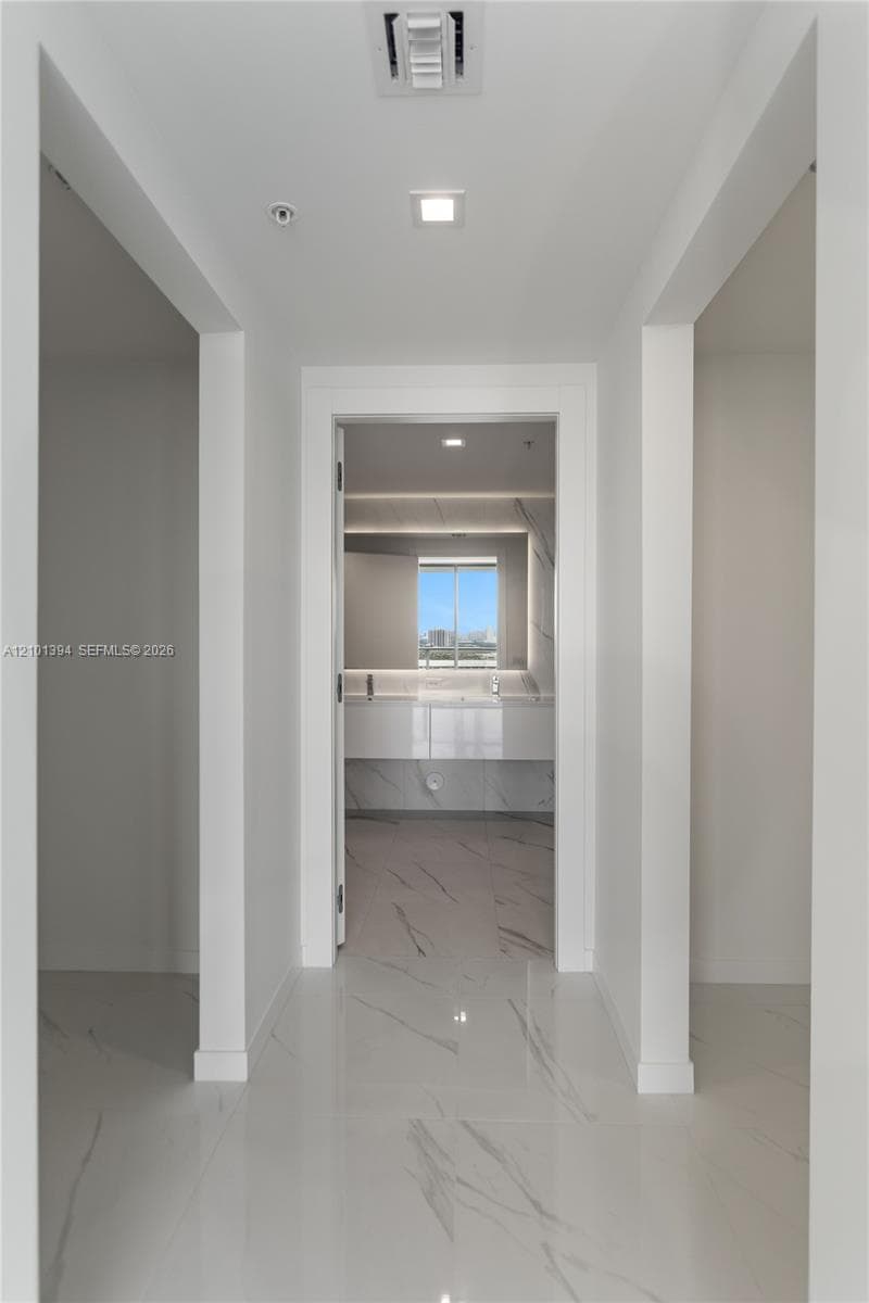 Hallway featuring polished stone-finish tile flooring, recessed ceiling lighting, and crisp white trim
