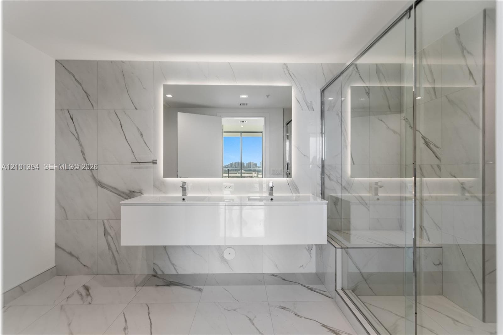 Floating dual-sink vanity with a solid-surface countertop, full-height stone-finish wall tiling, frameless glass-enclosed shower, and integrated backlit vanity mirror
