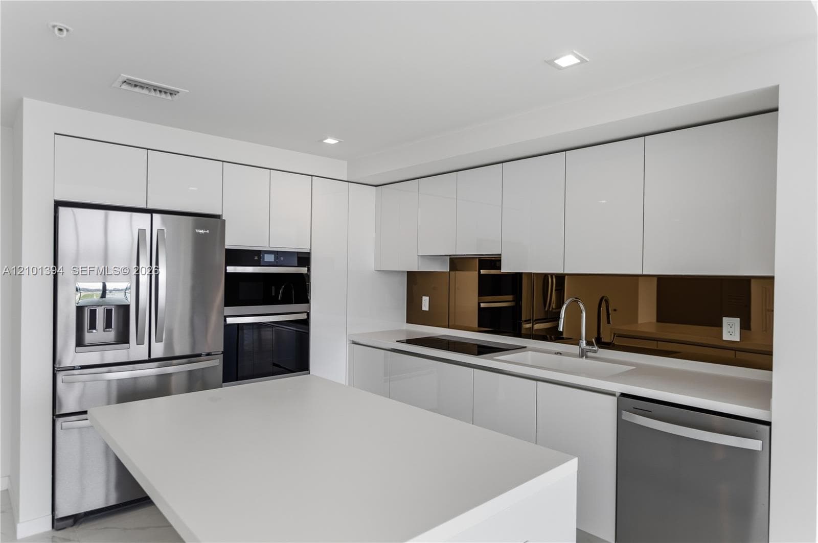 Kitchen featuring sleek white flat-panel cabinetry, quartz countertops, a bronze-toned mirrored backsplash, stainless steel appliances, and a central island with an integrated sink