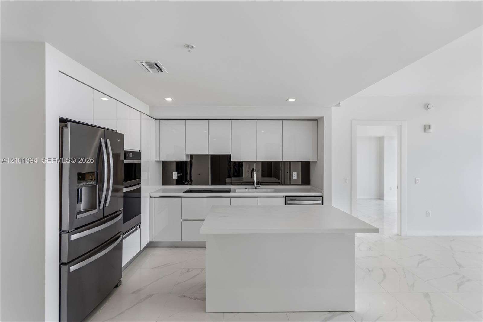 Modern kitchen featuring high-gloss white cabinetry, a center island with a solid surface countertop, stainless steel appliances, a dark mirrored backsplash, and stone-finish flooring