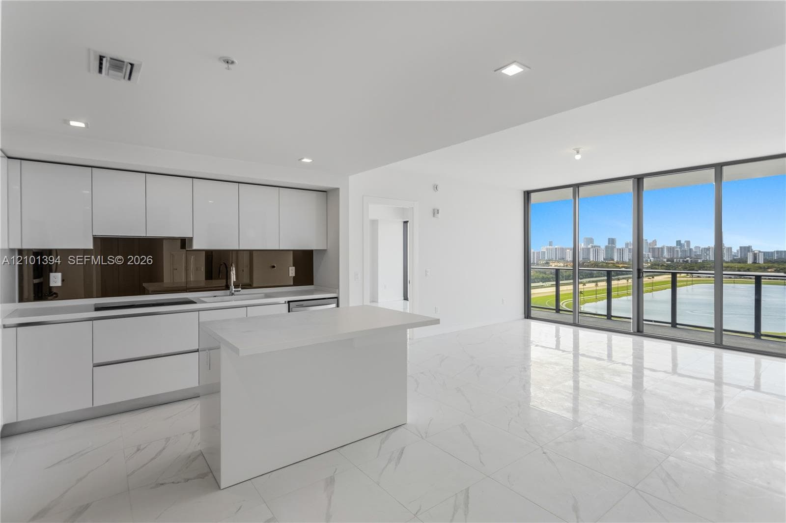 Modern kitchen featuring flat-panel white cabinetry, a center island with a stone-surface countertop, a mirrored backsplash, polished stone-finish floor tiling, and floor-to-ceiling windows