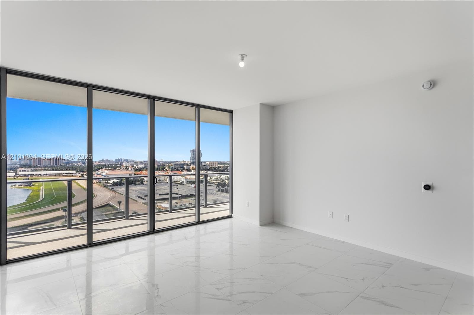 Floor-to-ceiling sliding glass doors, white large-format stone-finish tile flooring, and a private balcony featuring metal railing