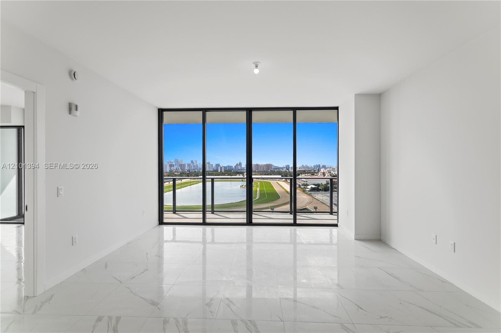 Open-concept room featuring polished stone-finish flooring, floor-to-ceiling glass sliding doors, and a covered balcony with a metal railing