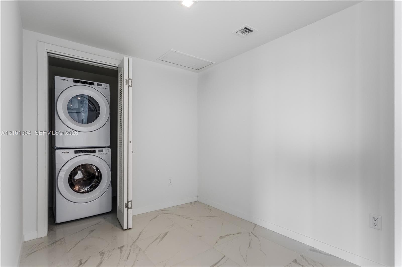 Laundry area featuring large-format tile flooring with marble-pattern veining and a stacked front-loading washer and dryer set