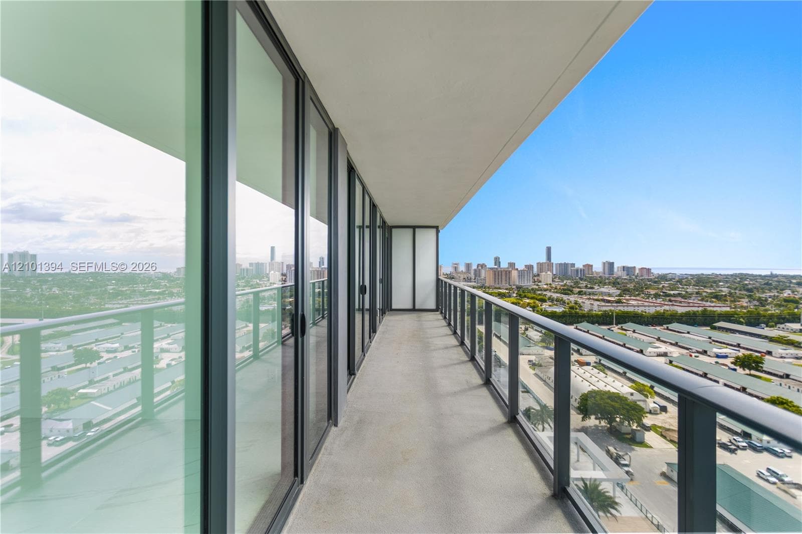 Covered balcony featuring full-height glass sliding doors, concrete flooring, and metal railings with glass panels