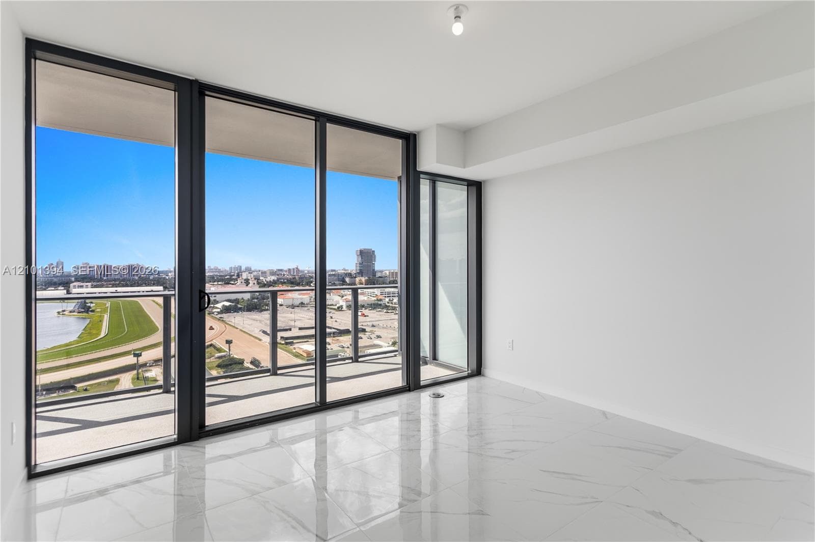 Floor-to-ceiling glass sliding doors, stone-finish tile flooring, and a private balcony with metal railings, featuring a cityscape and water horizon backdrop