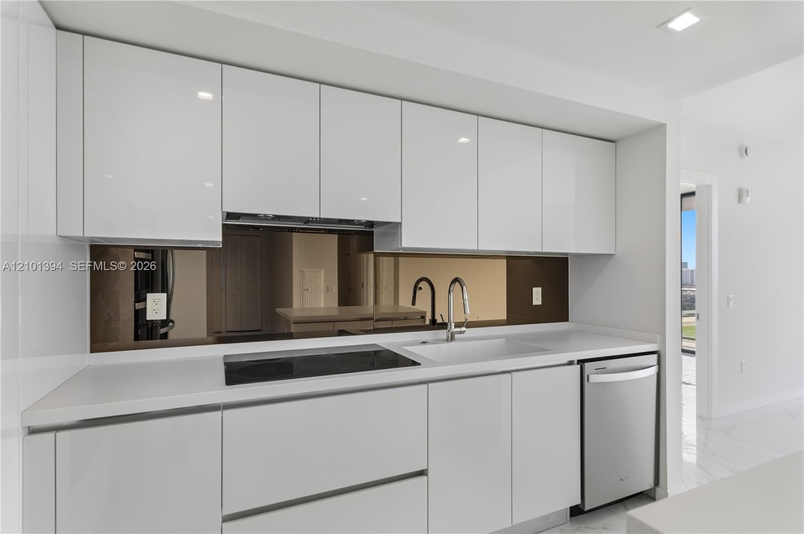 High-gloss white cabinetry, white solid-surface countertops, reflective backsplash, stainless steel dishwasher, and integrated cooktop