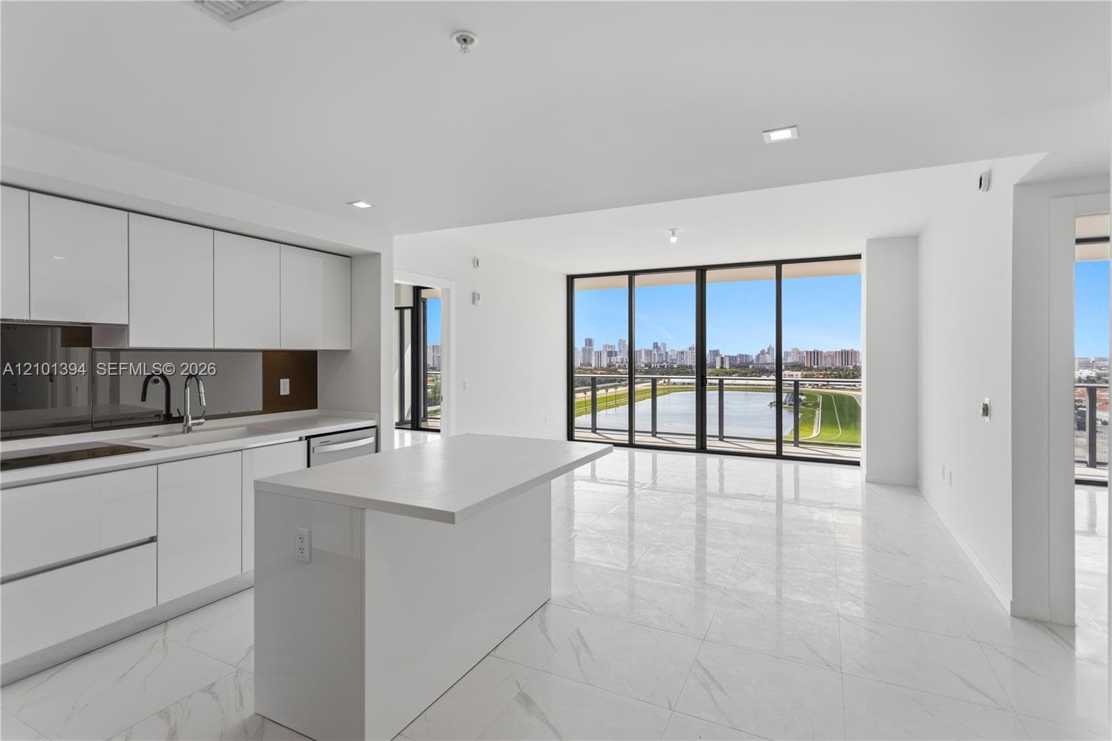 Contemporary kitchen featuring white flat-panel cabinetry, a stone-surface island, floor-to-ceiling windows, polished stone-finish flooring, and recessed lighting