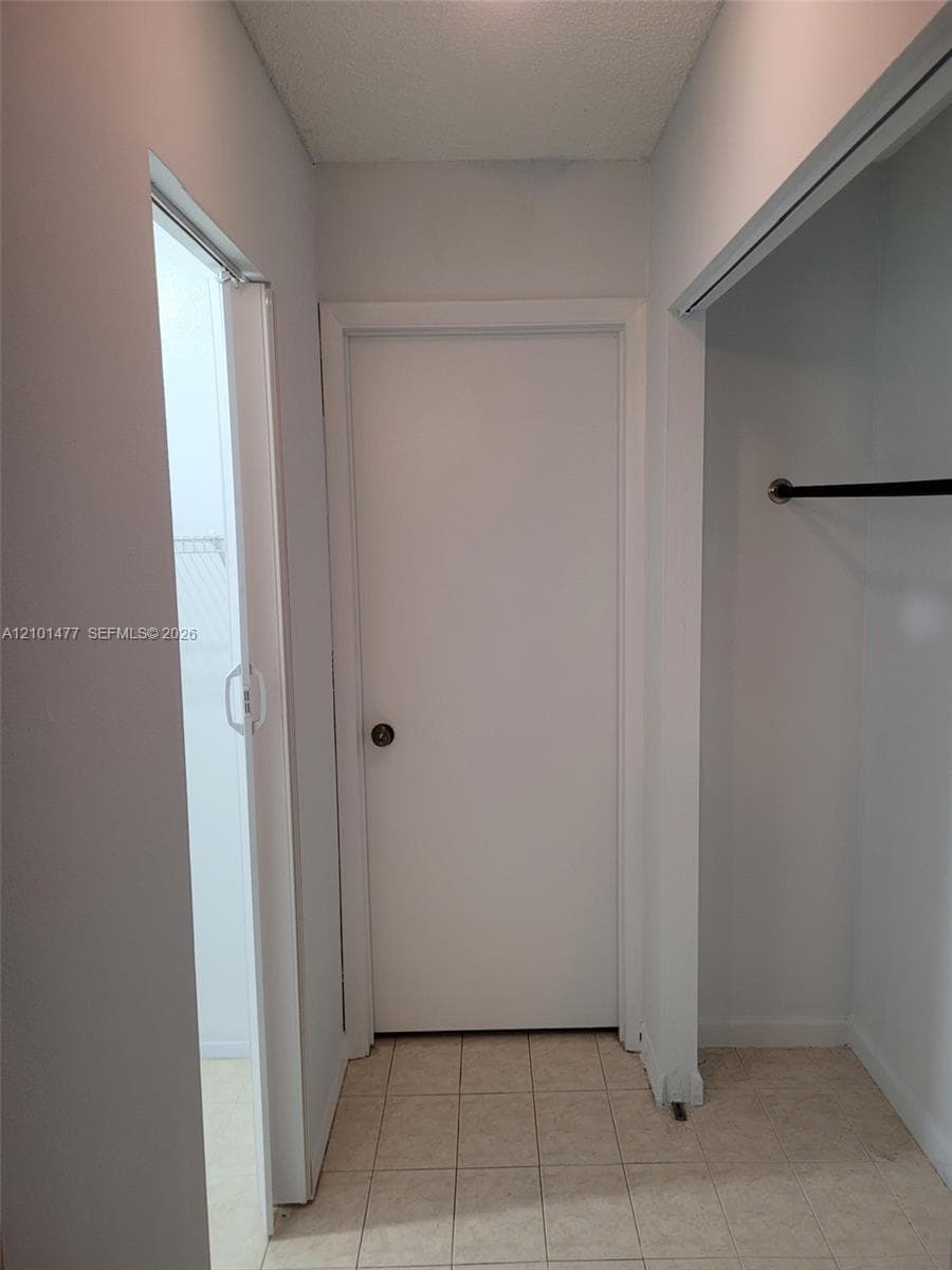 Neutral-toned interior featuring ceramic tile flooring, a centered solid-core door with a spherical knob, and a built-in closet with an integrated hanging rod