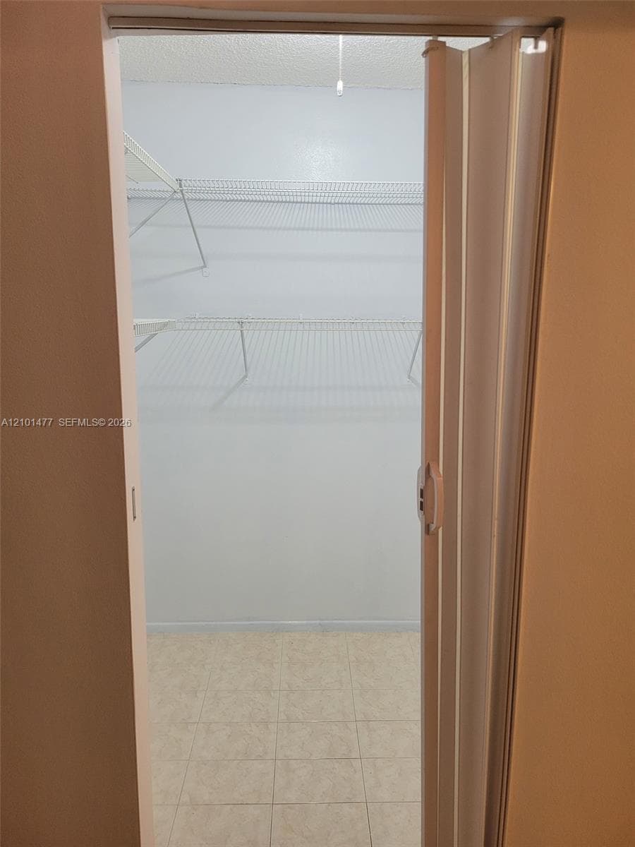 Storage space featuring white accordion doors, wire shelving units, and tile flooring