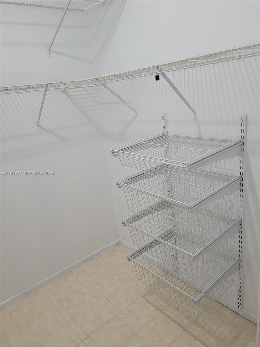 Storage closet featuring a white wire shelving system with four integrated slide-out wire baskets and wall-mounted support tracks over tile flooring
