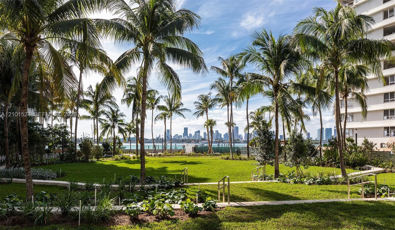 Manicured lawn featuring mature palm trees, multi-level hardscaped walkways with metal railings, and a skyline backdrop