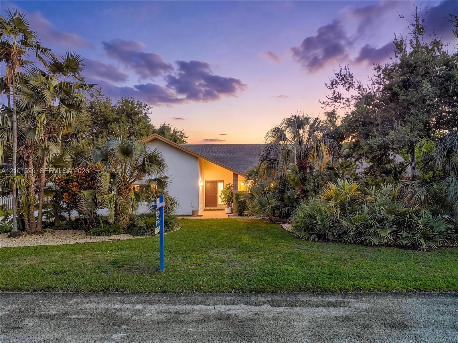 Pitched roofline, white exterior, mature palm trees, diverse landscaping, and a manicured lawn