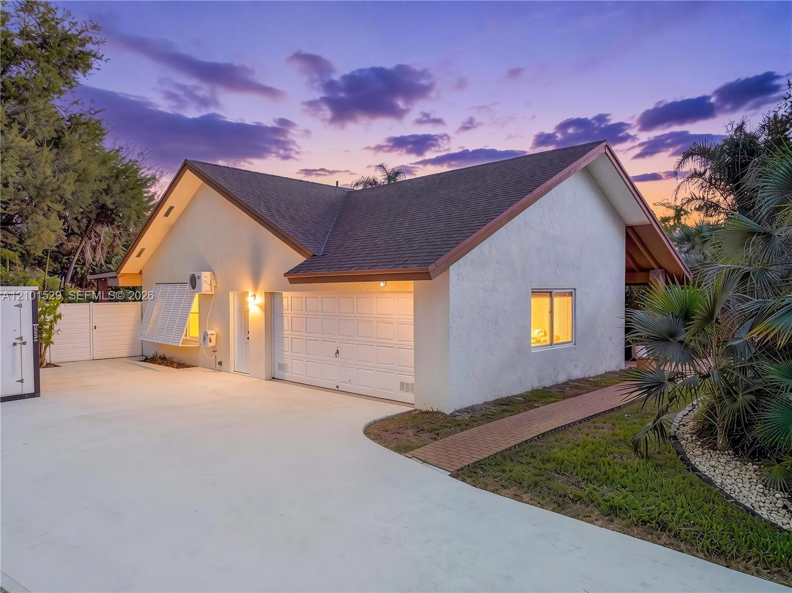 Stucco exterior with a peaked roof, attached garage, and a concrete driveway
