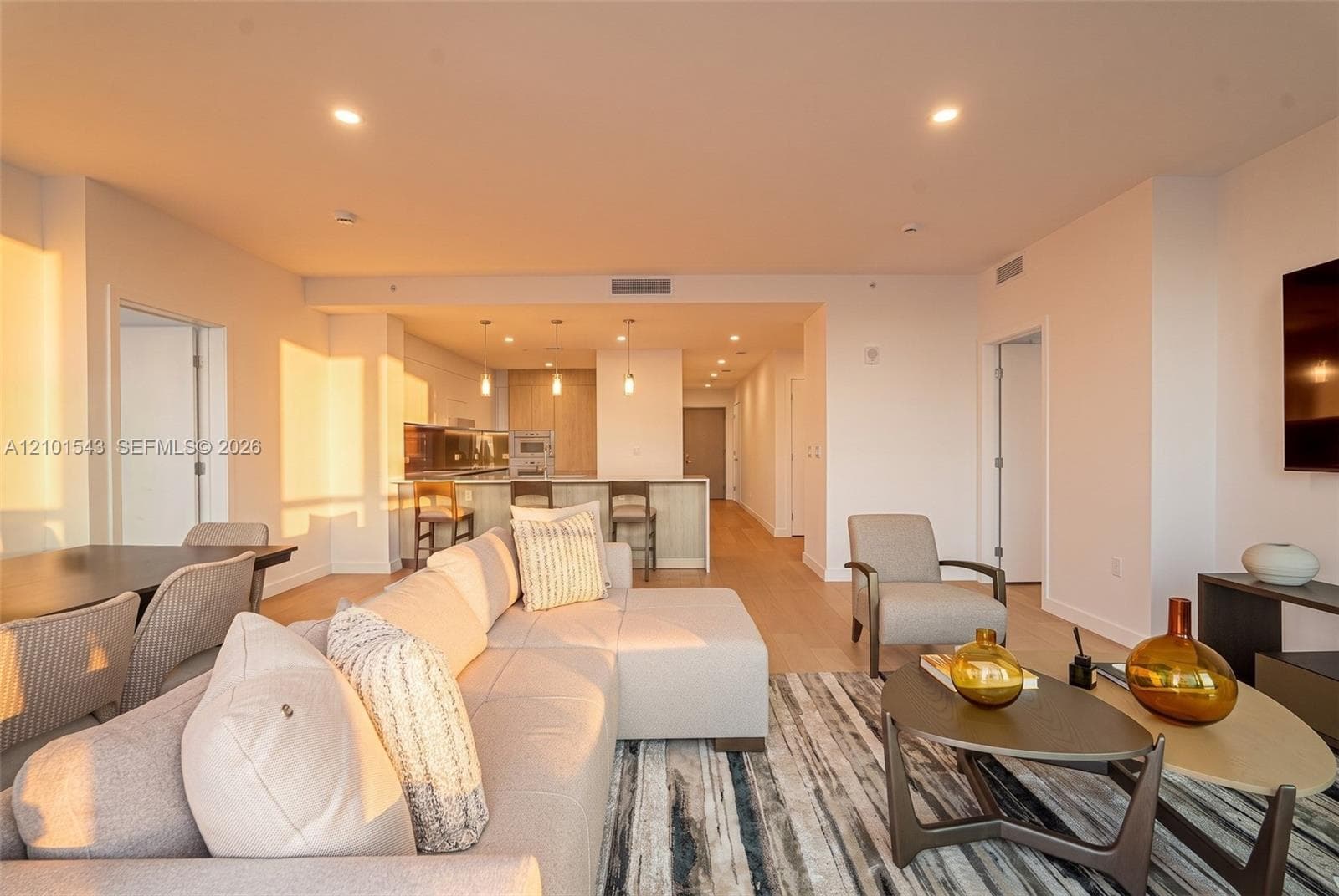 Open-concept living space featuring wood-finish flooring, recessed lighting, and a kitchen equipped with a stone-top island, built-in cabinetry, and multi-pendant lighting