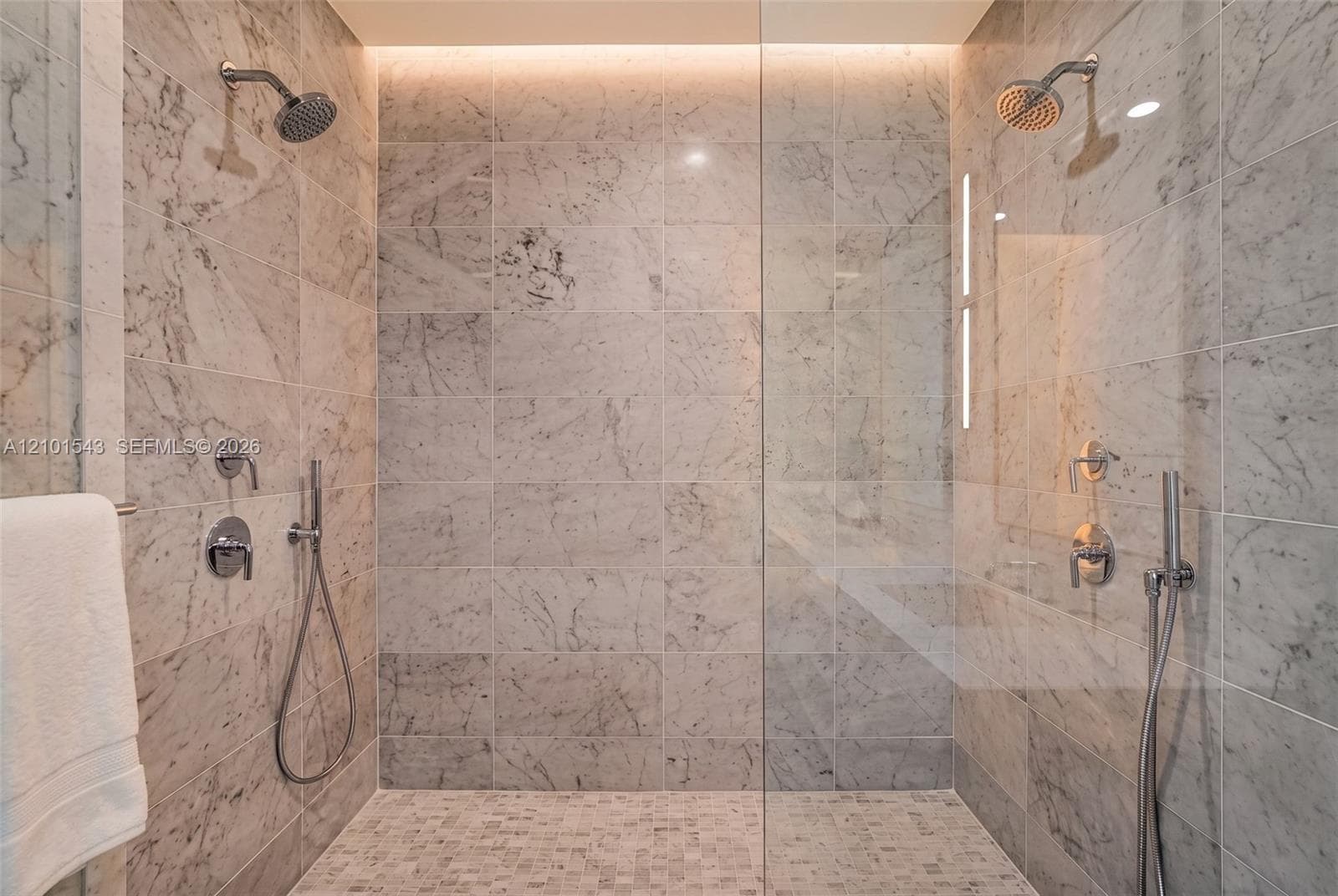 Walk-in shower featuring large-format stone wall tiling, mosaic stone flooring, dual shower heads with handheld sprayers, a frameless glass enclosure, and recessed overhead accent lighting