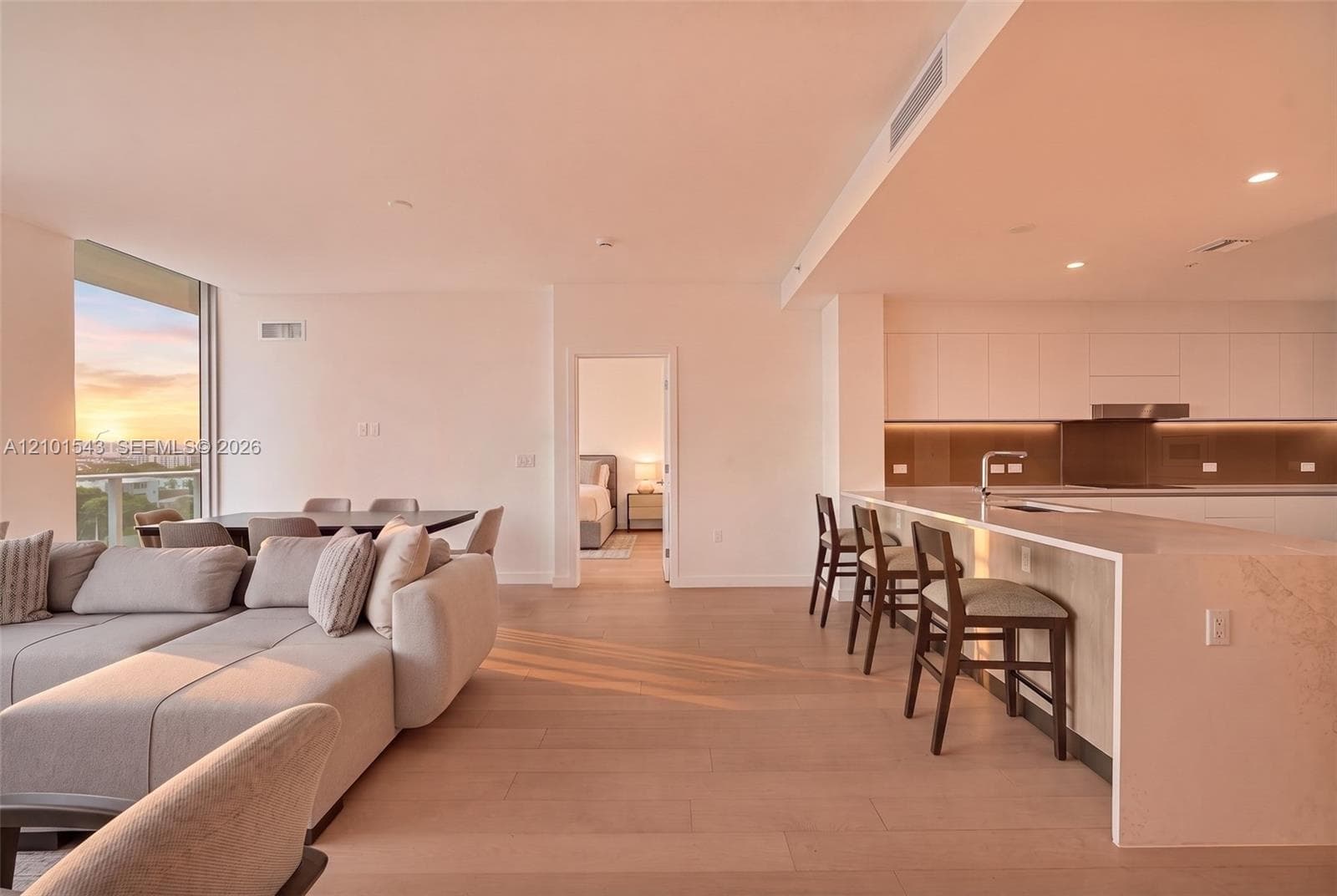 Open-concept interior featuring light wood-finish flooring, a kitchen with flat-panel cabinetry, a waterfall-edge countertop island, and recessed ceiling lighting