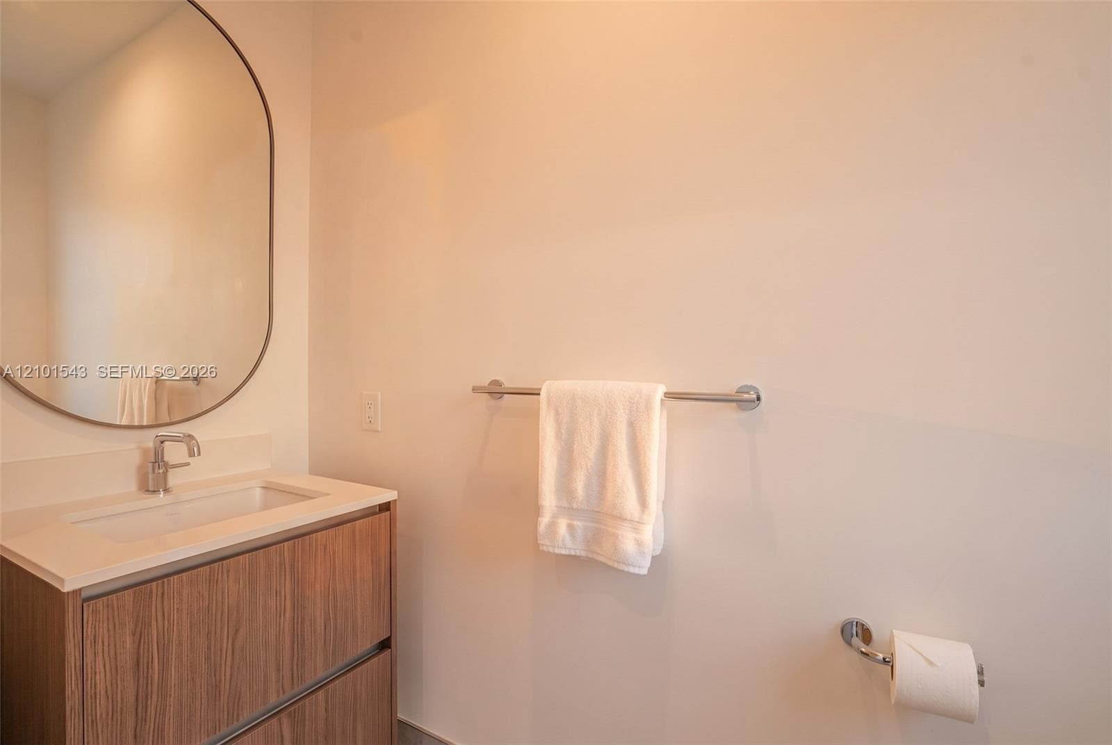 Wood-finish floating vanity with a stone-top integrated basin, polished chrome faucet, and oval wall-mounted mirror, complemented by matching chrome bathroom hardware