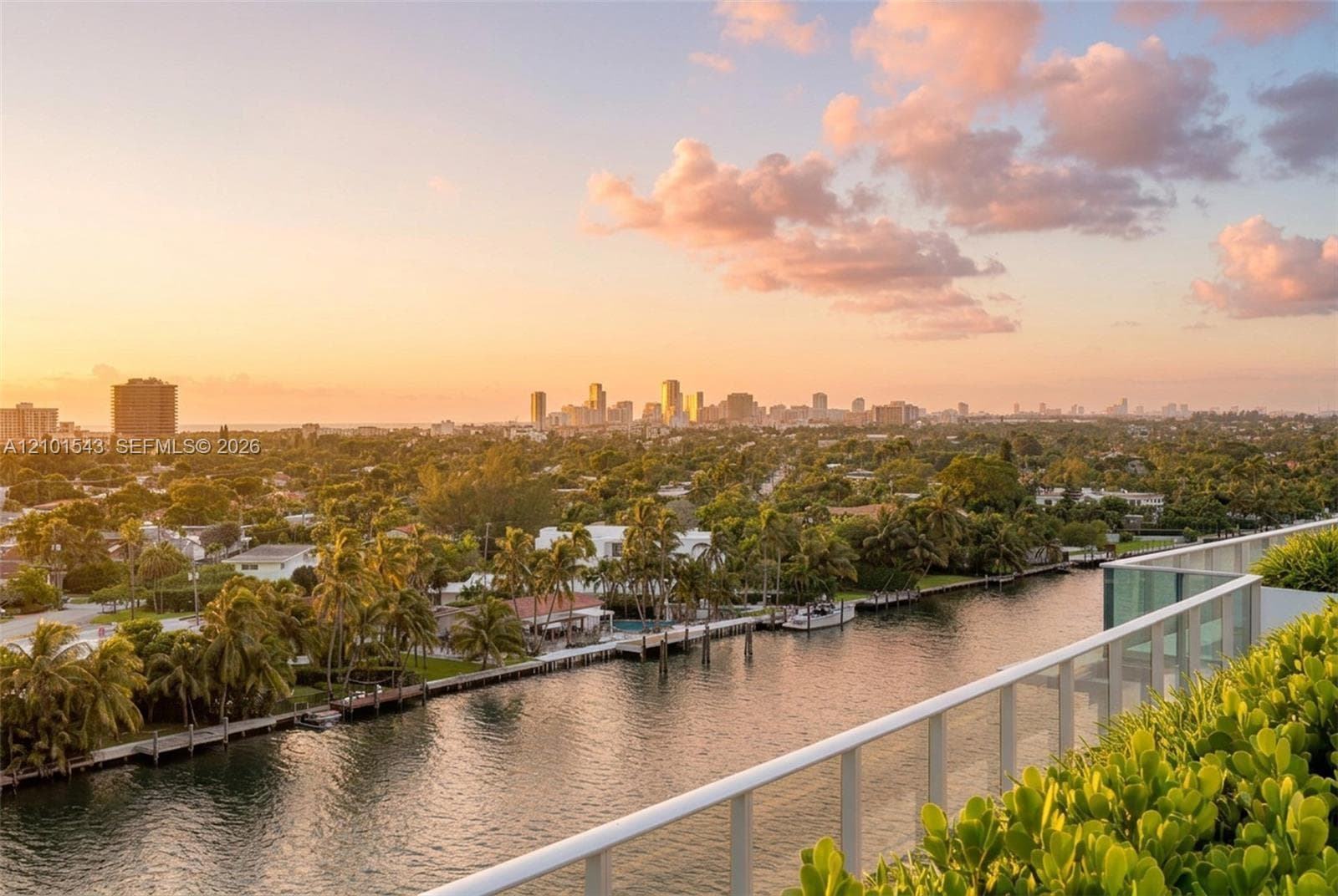 Elevated balcony featuring a glass panel railing, lush perimeter landscaping, and a panoramic perspective of the waterway and city skyline