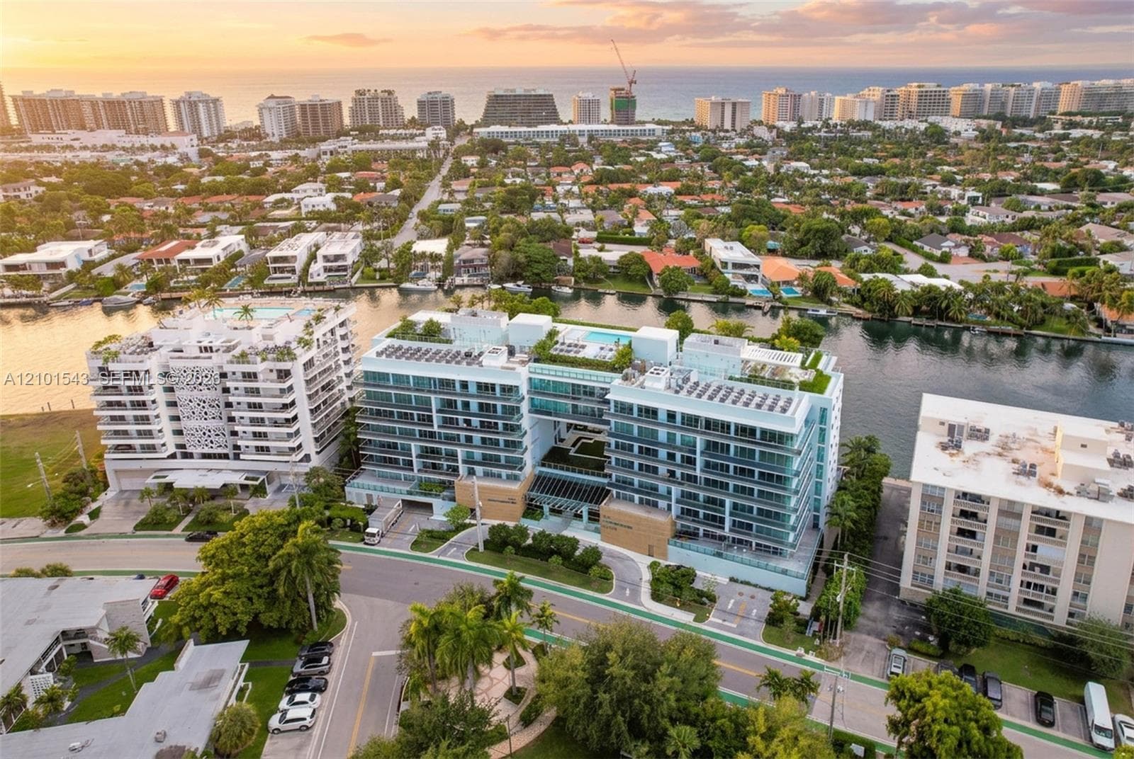 Multi-story mid-rise building featuring expansive glass balconies, a rooftop pool, landscaped green space, and direct water frontage
