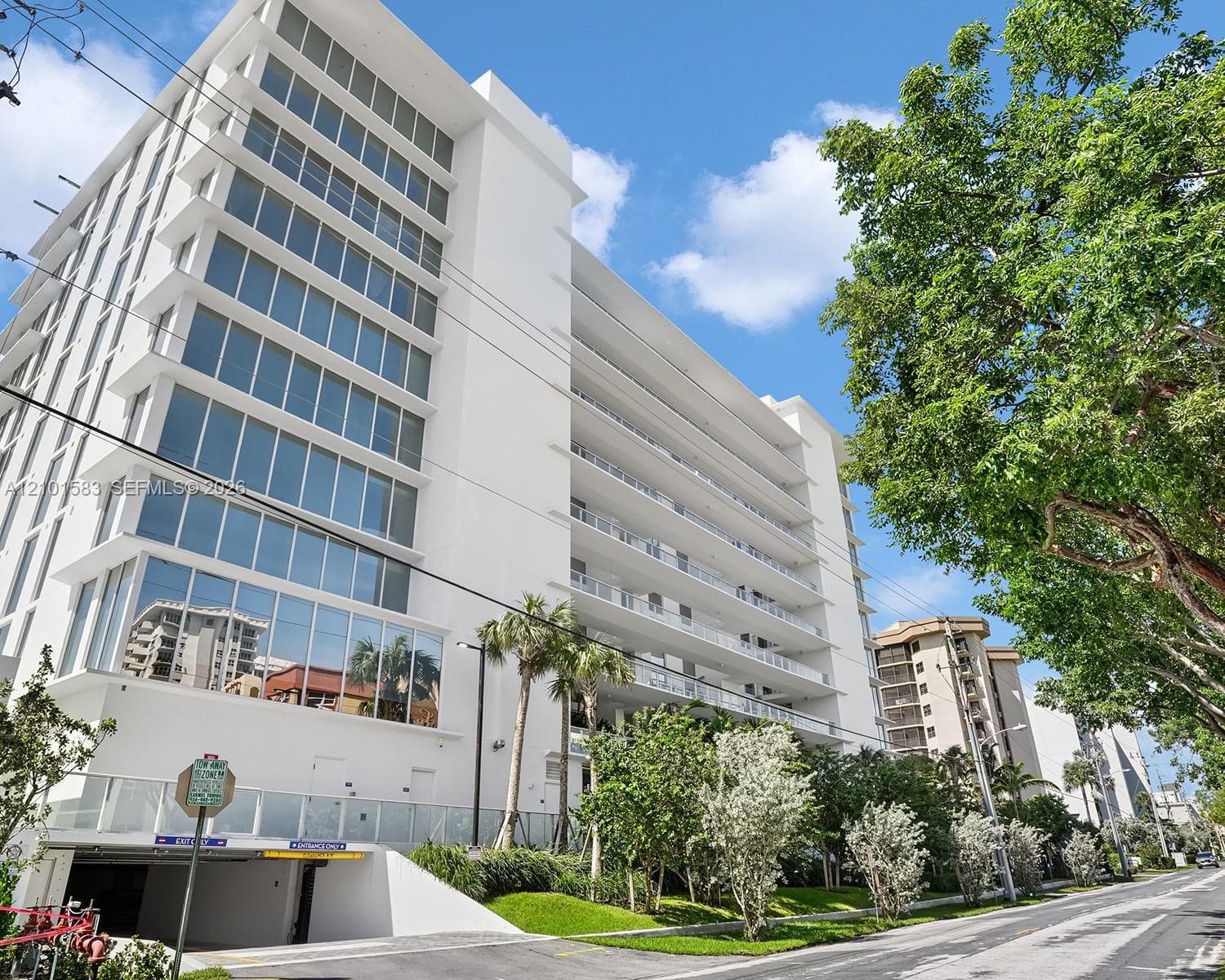 Mid-rise building exterior featuring full-height glass windows, private balconies with glass railings, and a subterranean garage entrance
