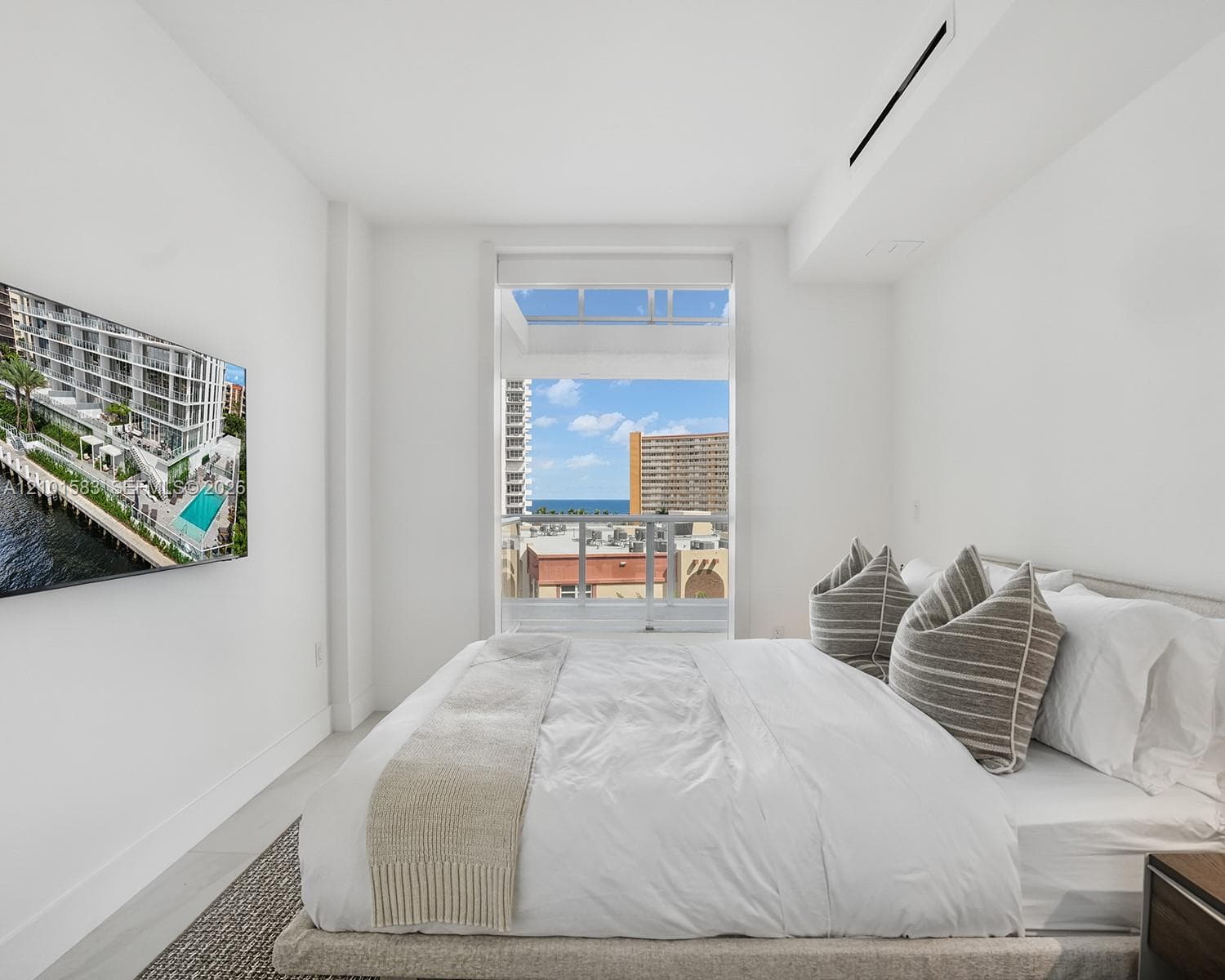 Floor-to-ceiling window featuring a glass balcony railing, neutral tile flooring, wall-mounted ductless climate control, and prominent water and cityscape scenery