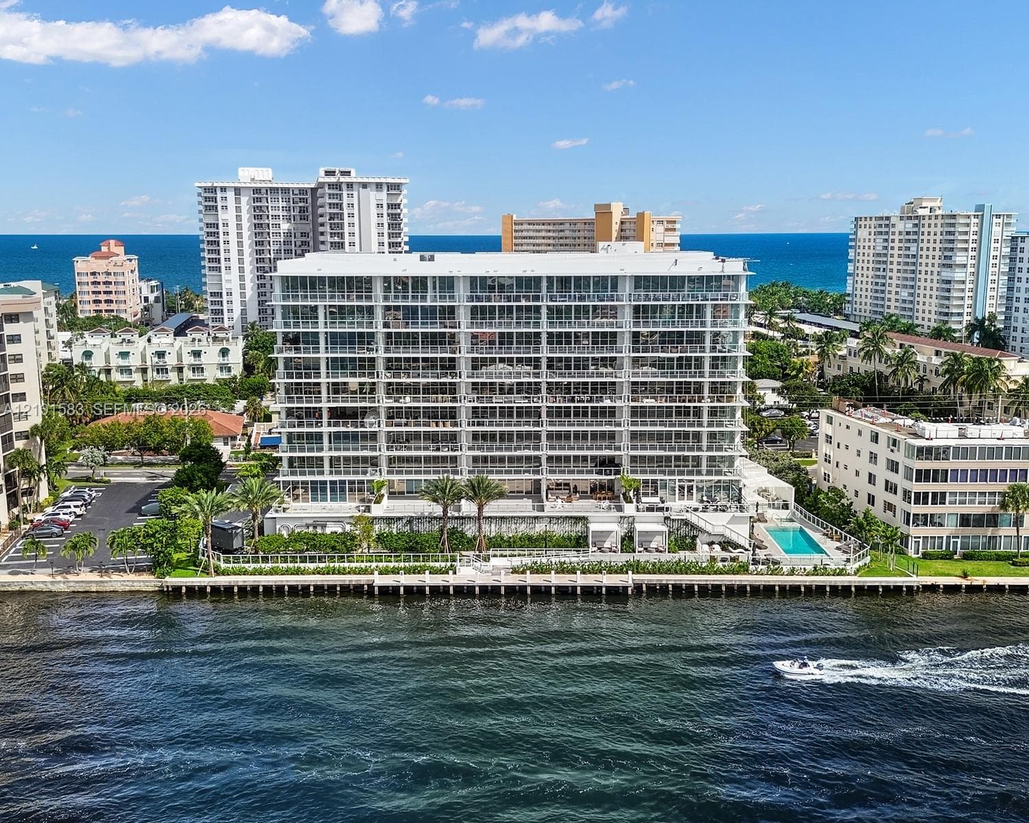 Waterfront multi-story residential building featuring floor-to-ceiling glass balconies, private dockage, a ground-level swimming pool, and manicured landscaping