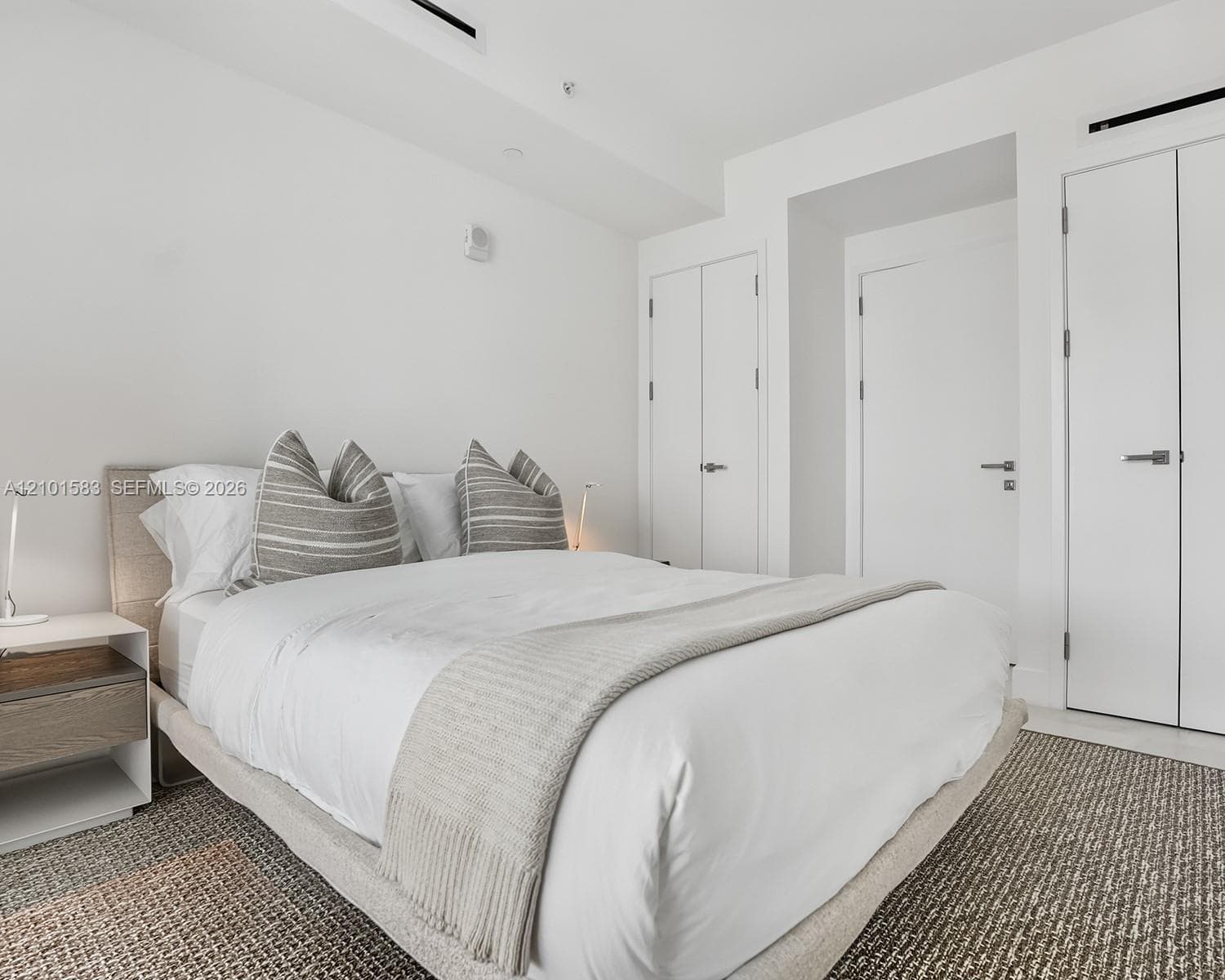 Neutral-toned interior space featuring crisp white walls, recessed ceiling lighting, and multiple floor-to-ceiling closets with minimalist hardware