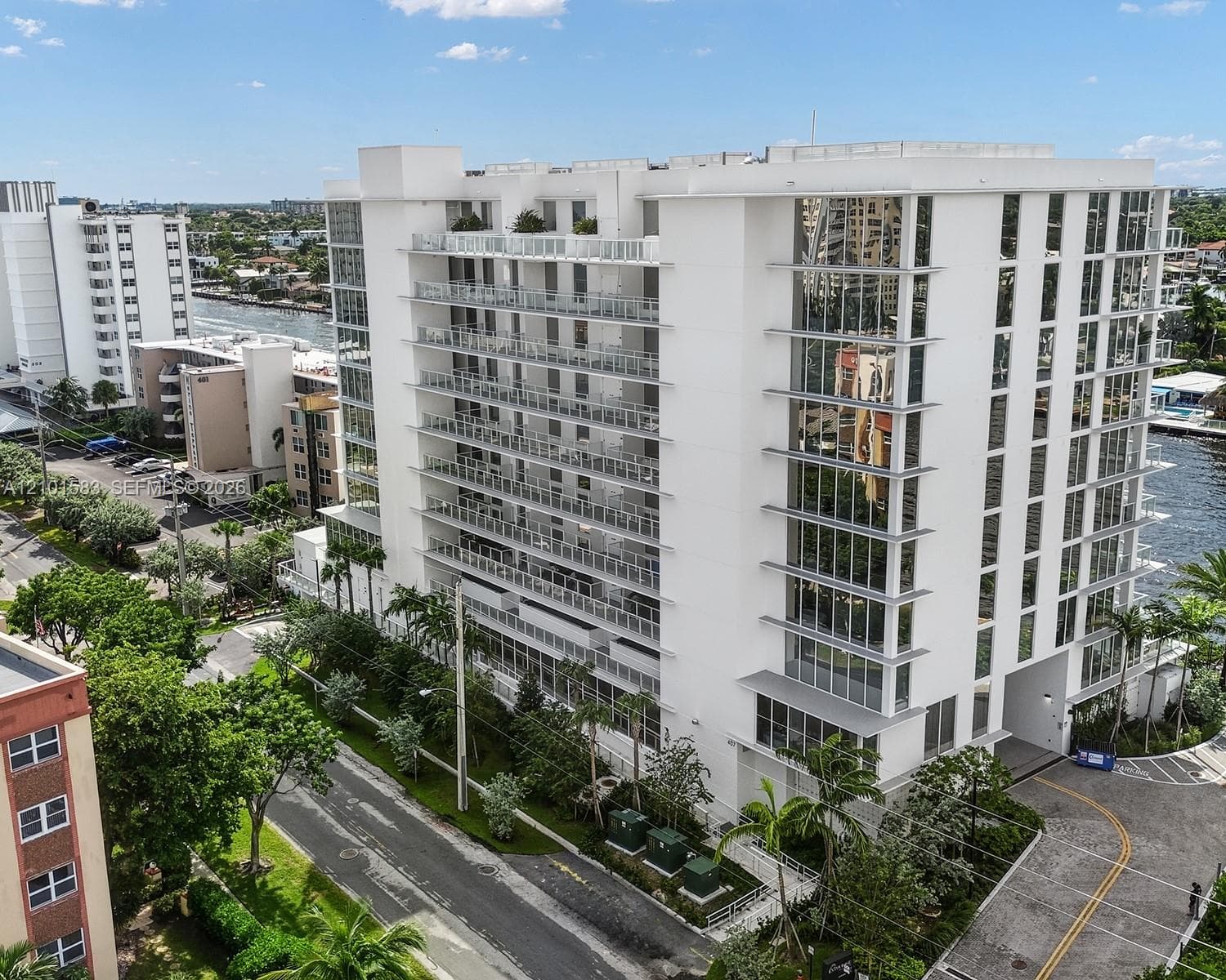 Mid-rise building featuring a white facade, extensive glass paneling, multiple levels of private balconies with railings, and waterfront positioning