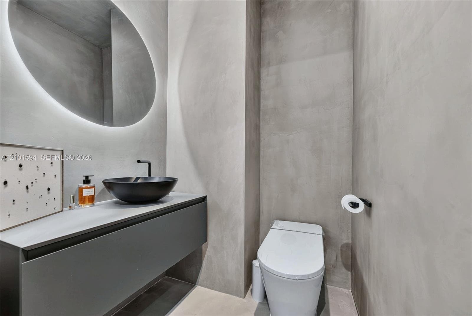 Powder room with floating vanity, vessel sink and round backlit mirror.