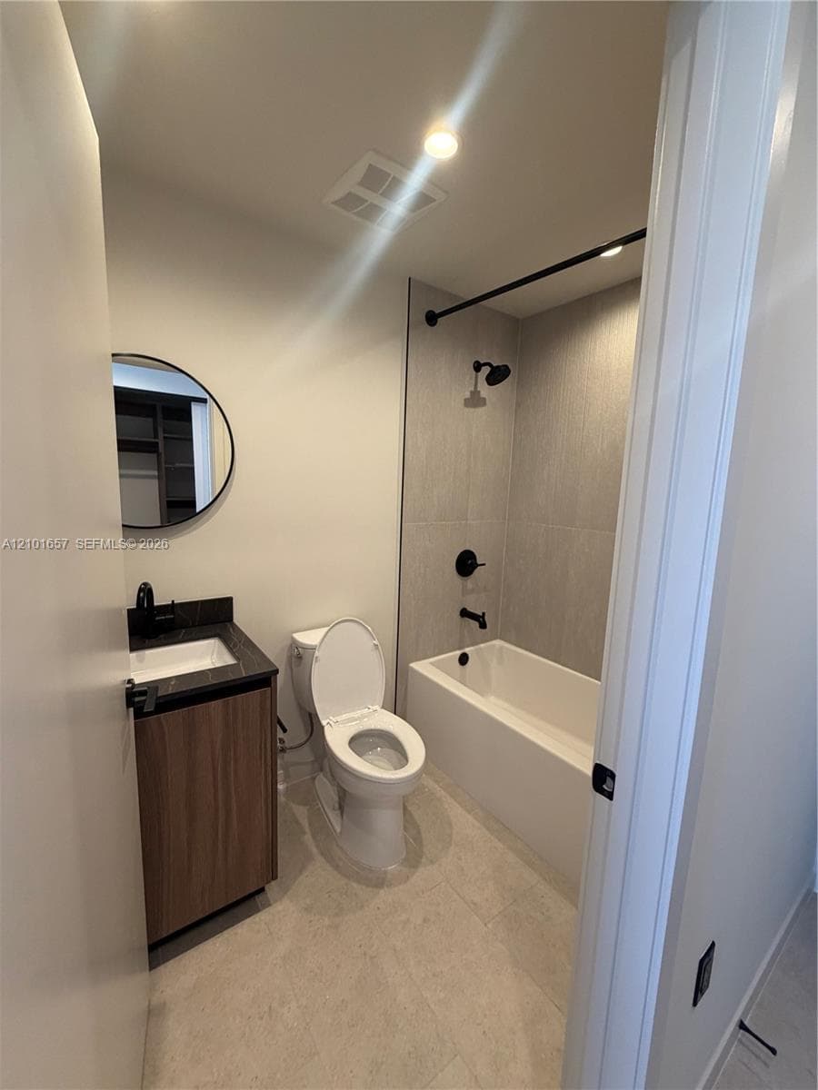 Bathroom featuring a wood-finish vanity with a dark stone countertop, circular mirror, and matte black hardware including a shower-tub faucet assembly with full-height tile surround